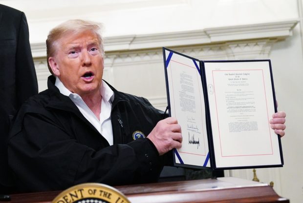 US President Donald Trump holds up an USD 8 billion emergency funding bill to combat COVID-19, coronavirus, after signing it in the Diplomatic Room of the White House in Washington, DC on March 6, 2020. (Photo by MANDEL NGAN / AFP) (Photo by MANDEL NGAN/AFP via Getty Images)