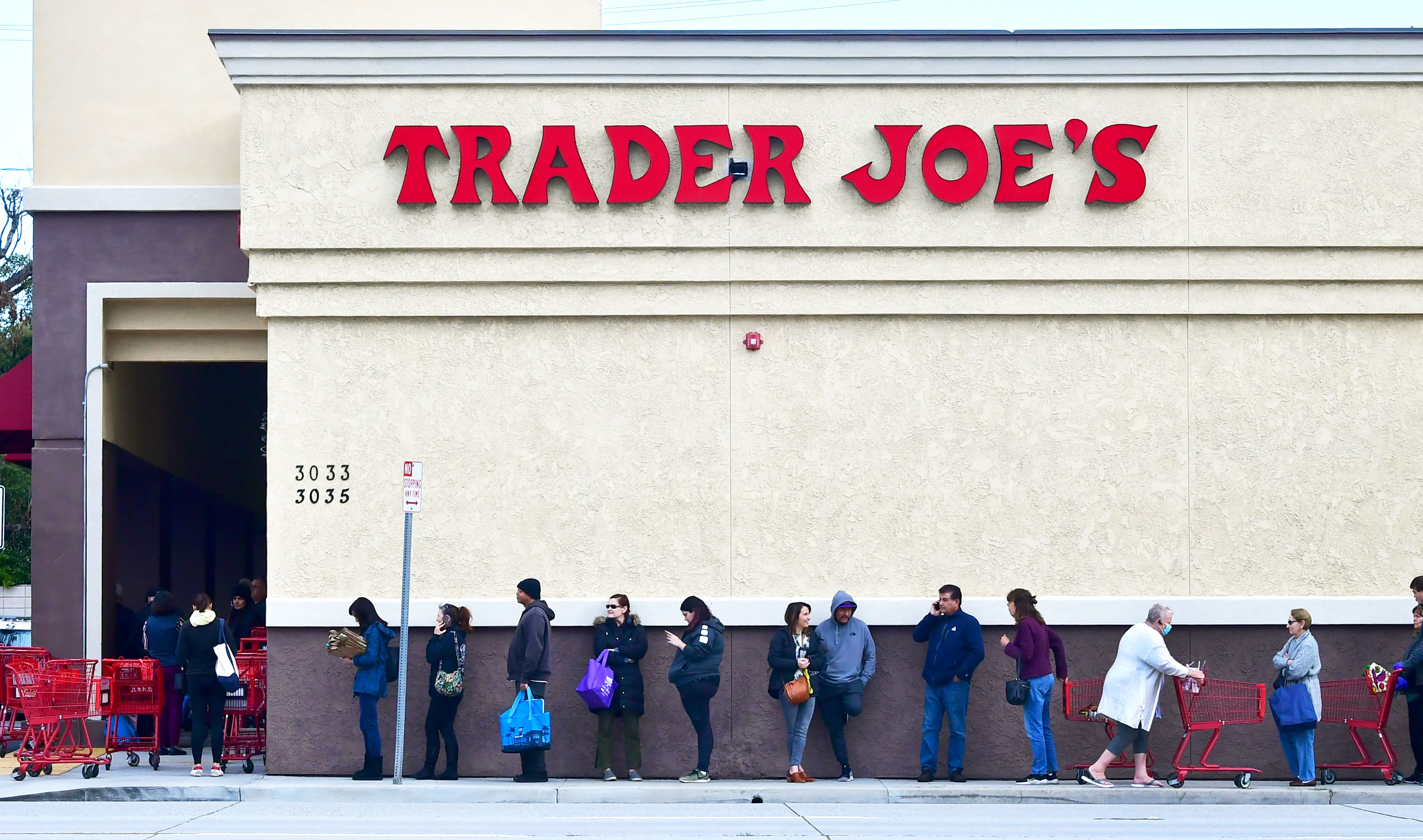A woman wearing a facemask pushes her cart to the back of the line as people line up before the opening of a Trader Joe's store in Pasadena, Caifornia on March 18, 2020 (Photo by FREDERIC J. BROWN/AFP via Getty Images)