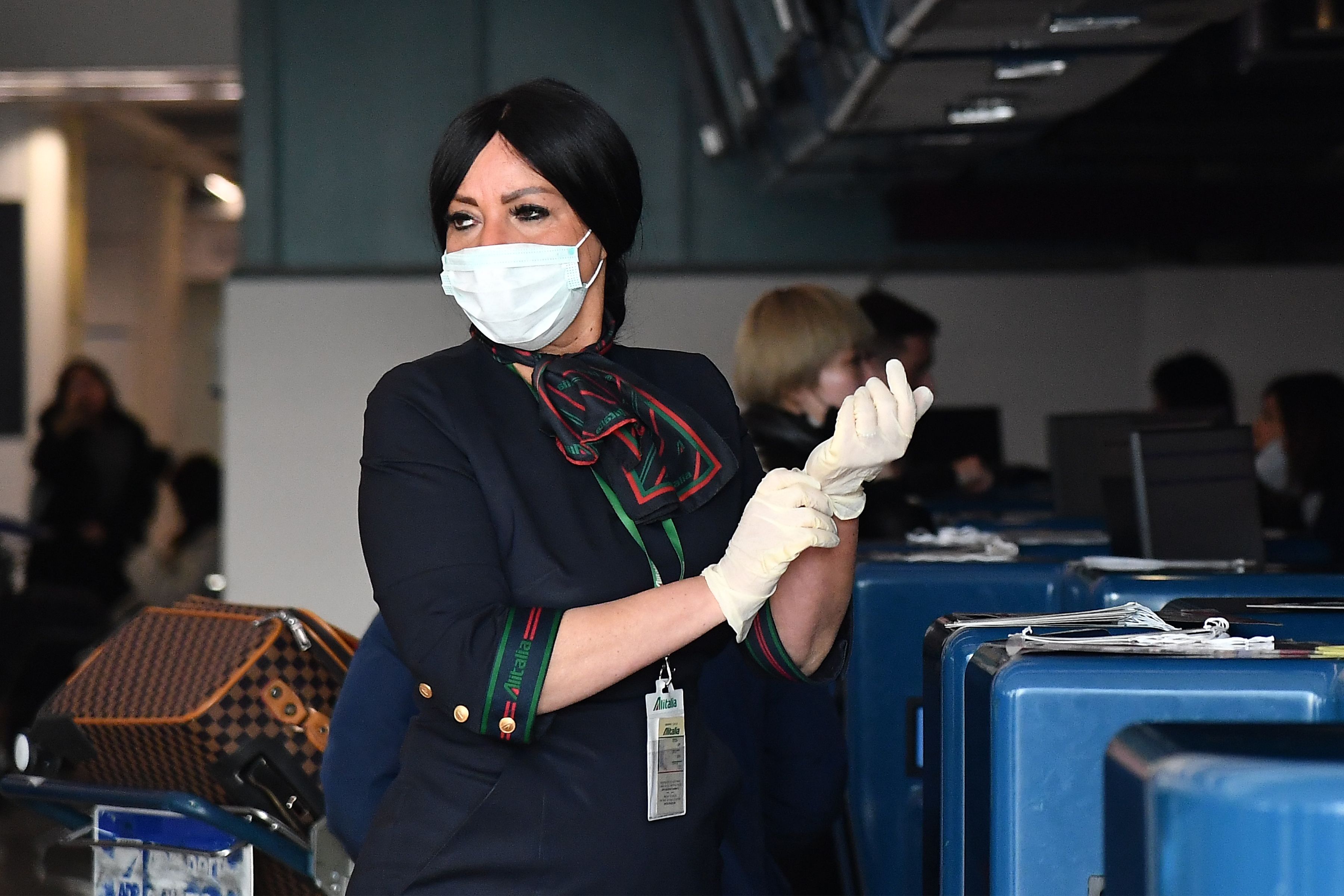 An airport employee puts on protective gloves and respiratory mask as she prepares to do passengers' check in at the counter of China Southern Airlines at Rome's Fiumicino airport, for a flight returning to Wuhan, China. (Photo by TIZIANA FABI/AFP via Getty Images)