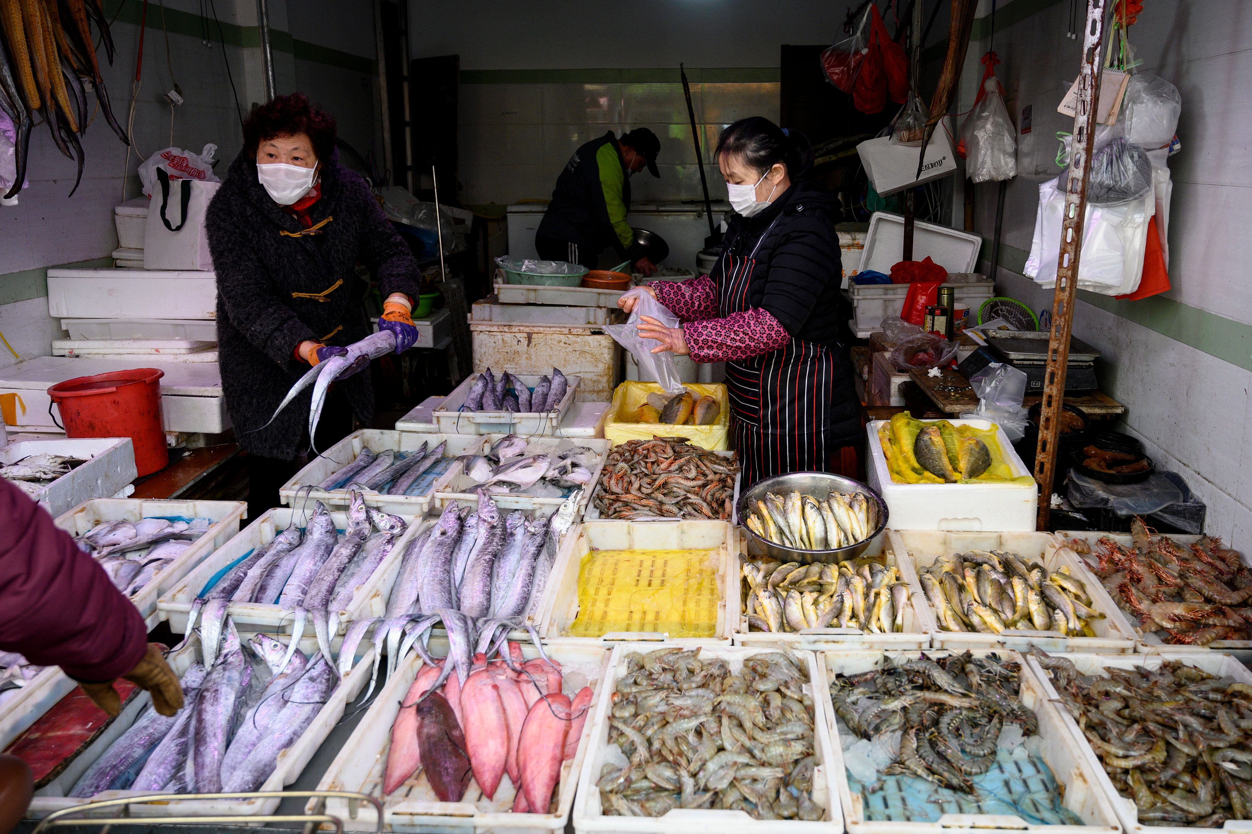 A seafood vendor (R) wearing a face mask talks to a customer at a wet market in Shanghai on February 13, 2020. (Photo by NOEL CELIS/AFP via Getty Images)