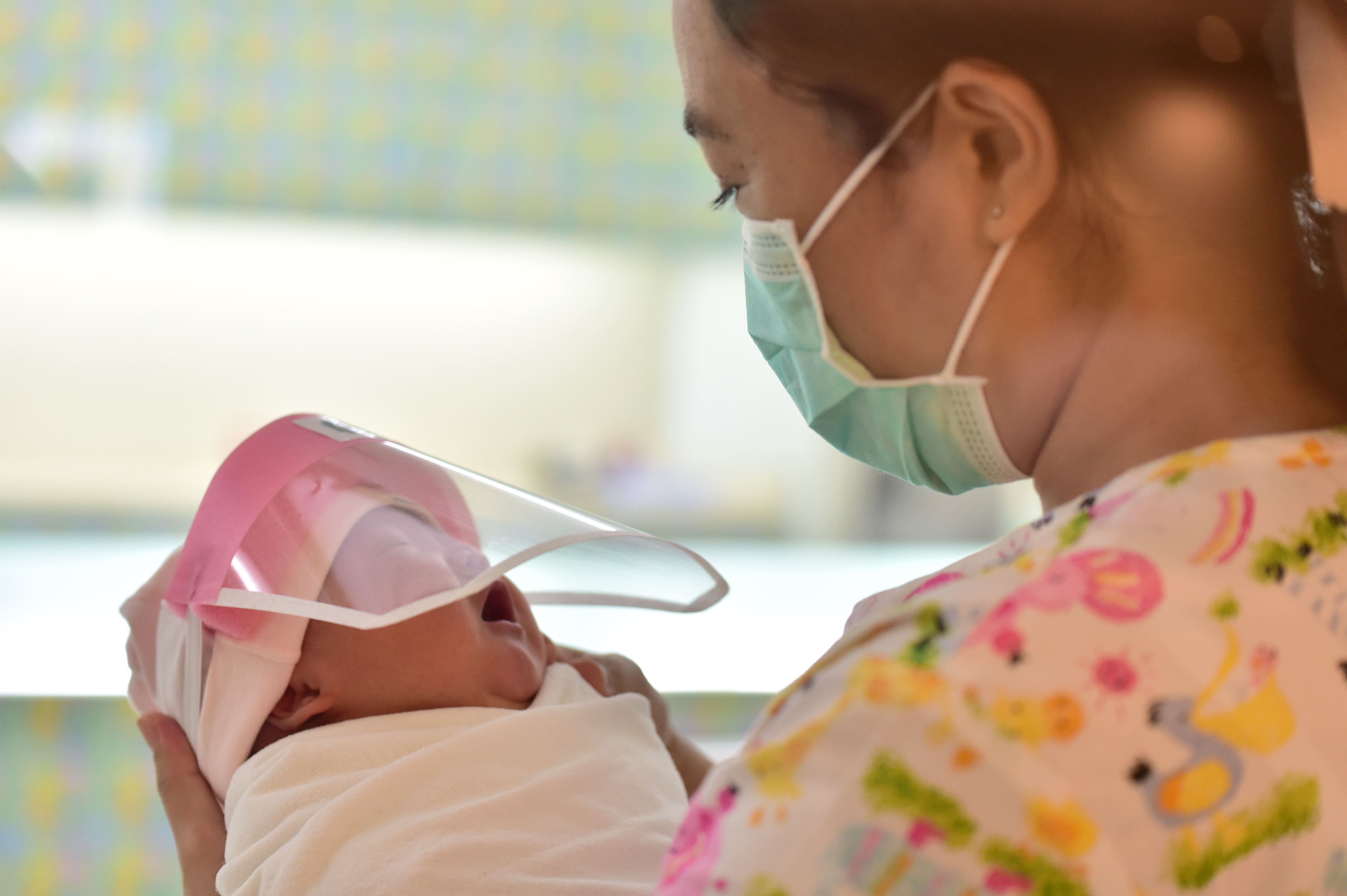 This photo taken through a glass window at a maternity ward shows a nurse holding a newborn baby wearing a face shield, in an effort to halt the spread of the COVID-19 coronavirus, at Praram 9 Hospital in Bangkok on April 9, 2020. (Photo by Lillian SUWANRUMPHA / AFP) (Photo by LILLIAN SUWANRUMPHA/AFP via Getty Images)
