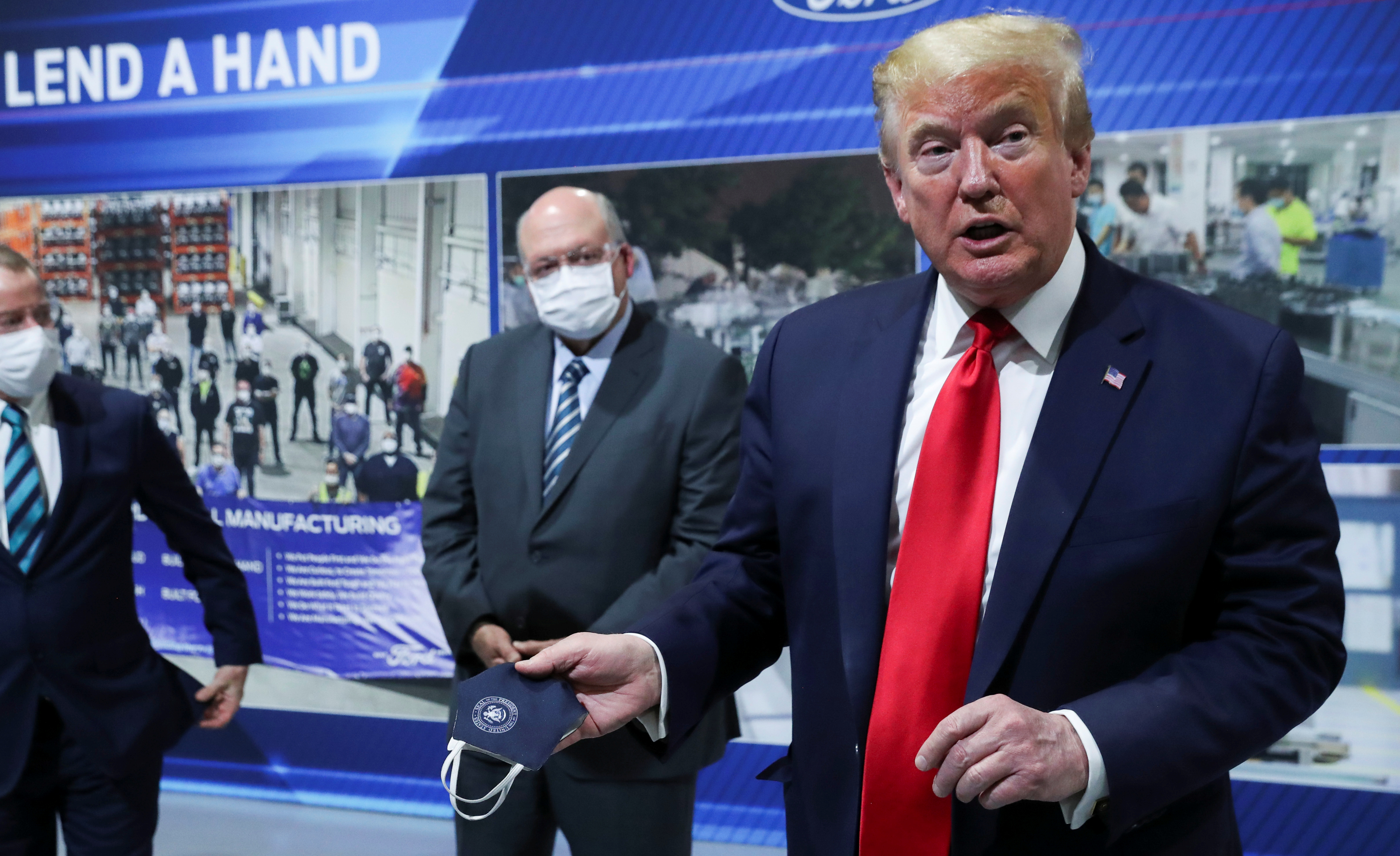 U.S. President Donald Trump holds a protective face mask with a presidential seal on it that he said he had been wearing earlier in his tour as Ford Motor Company CEO Jim Hackett looks on at the Ford Rawsonville Components Plant that is manufacturing ventilators, masks and other medical supplies during the coronavirus disease (COVID-19) pandemic in Ypsilanti, Michigan, U.S., May 21, 2020. REUTERS/Leah Millis