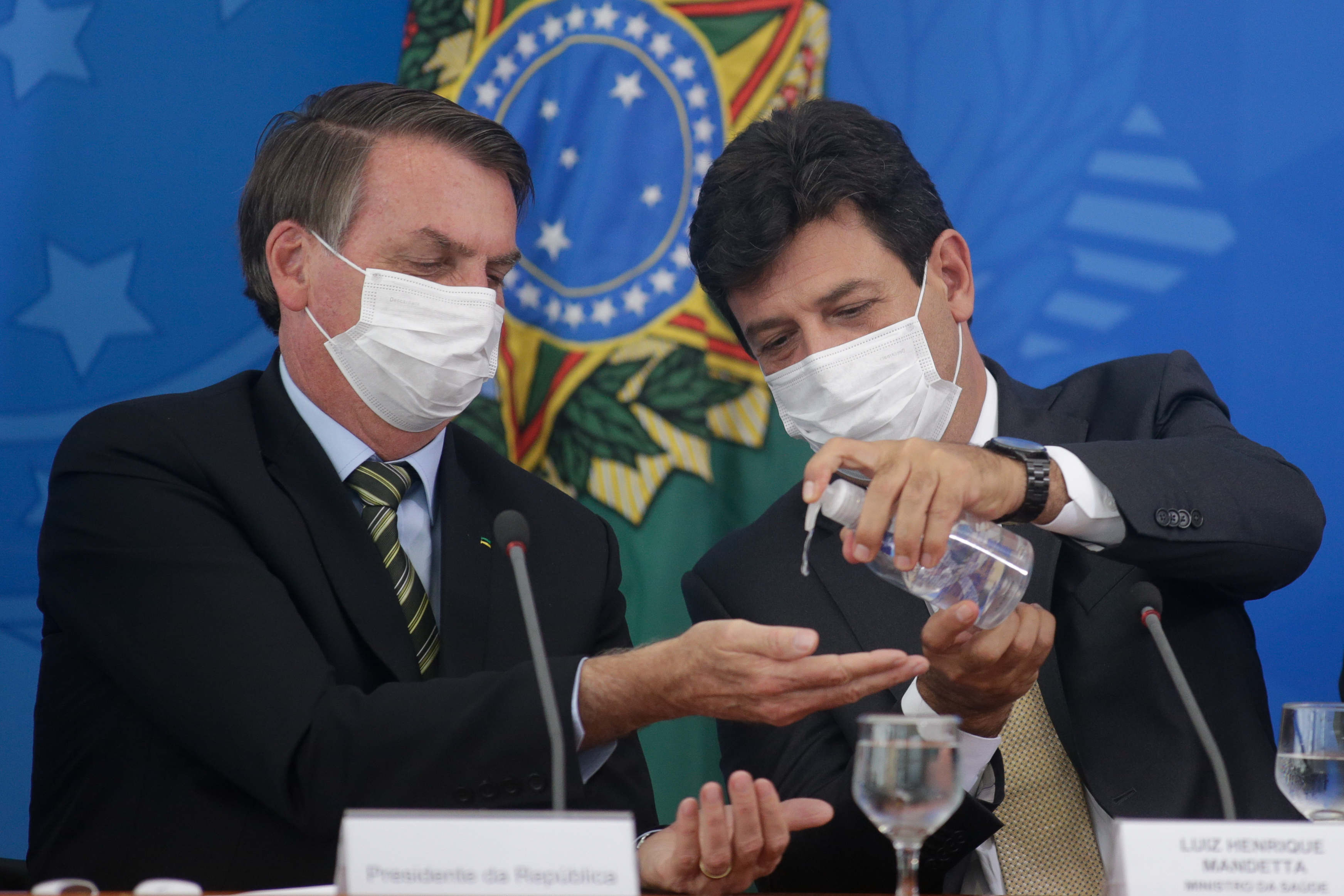 Brazilian Health Minister Luiz Henrique Mandetta (R) gives gel alcohol to President of Brazil Jair Bolsonaro, both using protective masks, during a press conference regarding government plans and measures on Coronavirus (COVID-19) Outbreak in Brazil, at the Planalto Palace on March 18, 2020 in Brasilia, Brazil. (Photo by Andre Coelho/Getty Images)