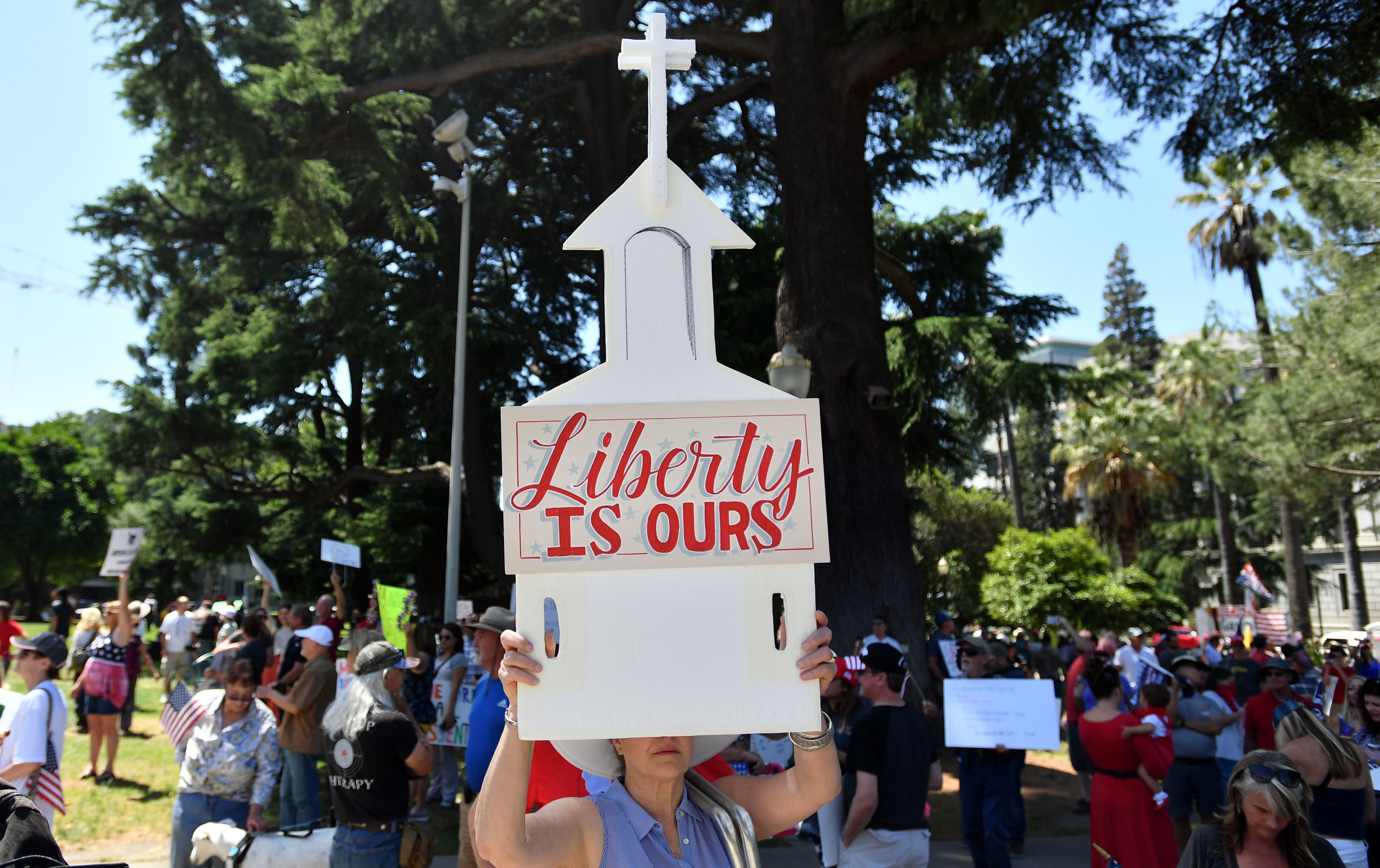 A woman holds up a sign depicting a church as hundreds of people gather to protest the stay-at-home orders outside the state capitol building in Sacramento, California on May 01, 2020. (Photo by JOSH EDELSON/AFP via Getty Images)