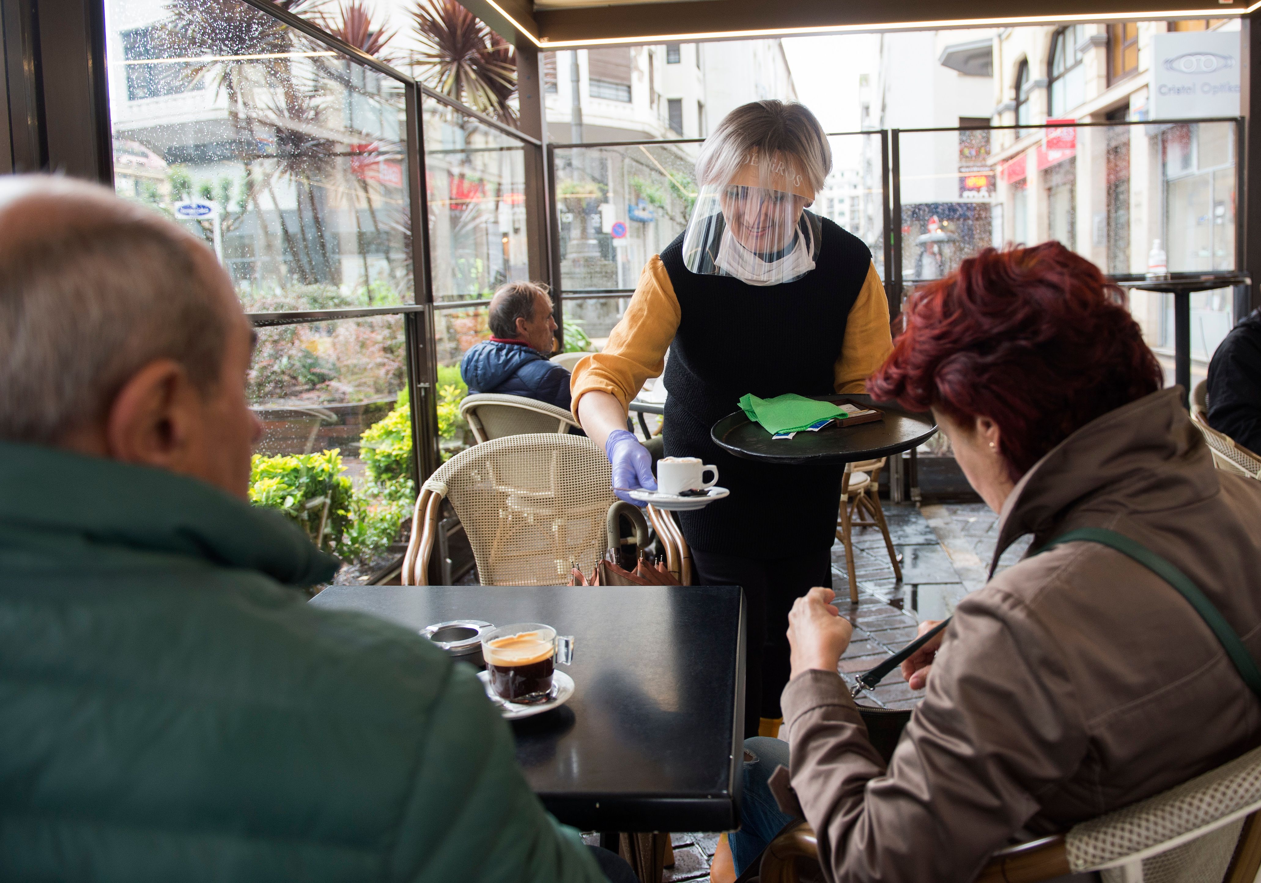 An employee serves coffee wearing a face shield and gloves at a cafeteria in the Spanish Basque city of San Sebastian on May 11, 2020. (Photo by ANDER GILLENEA/AFP via Getty Images)