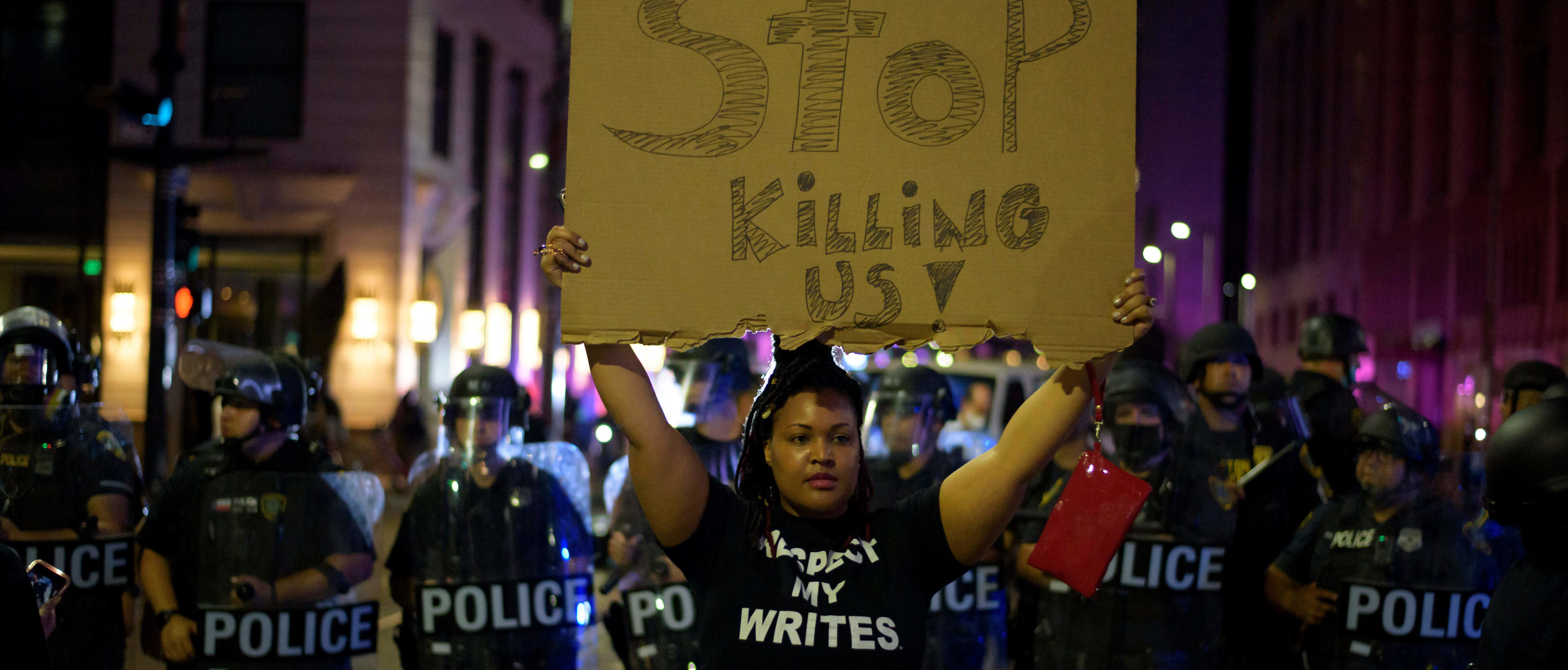 A protester holds up a sign with a row of police officers behind during a "Justice 4 George Floyd" demonstration over the death of George Floyd, a black man who died after a white policeman kneeled on his neck for several minutes in Houston, Texas on May 29, 2020. - Demonstrations are being held across the US after George Floyd died in police custody on May 25. (Photo by MARK FELIX/AFP /AFP via Getty Images)