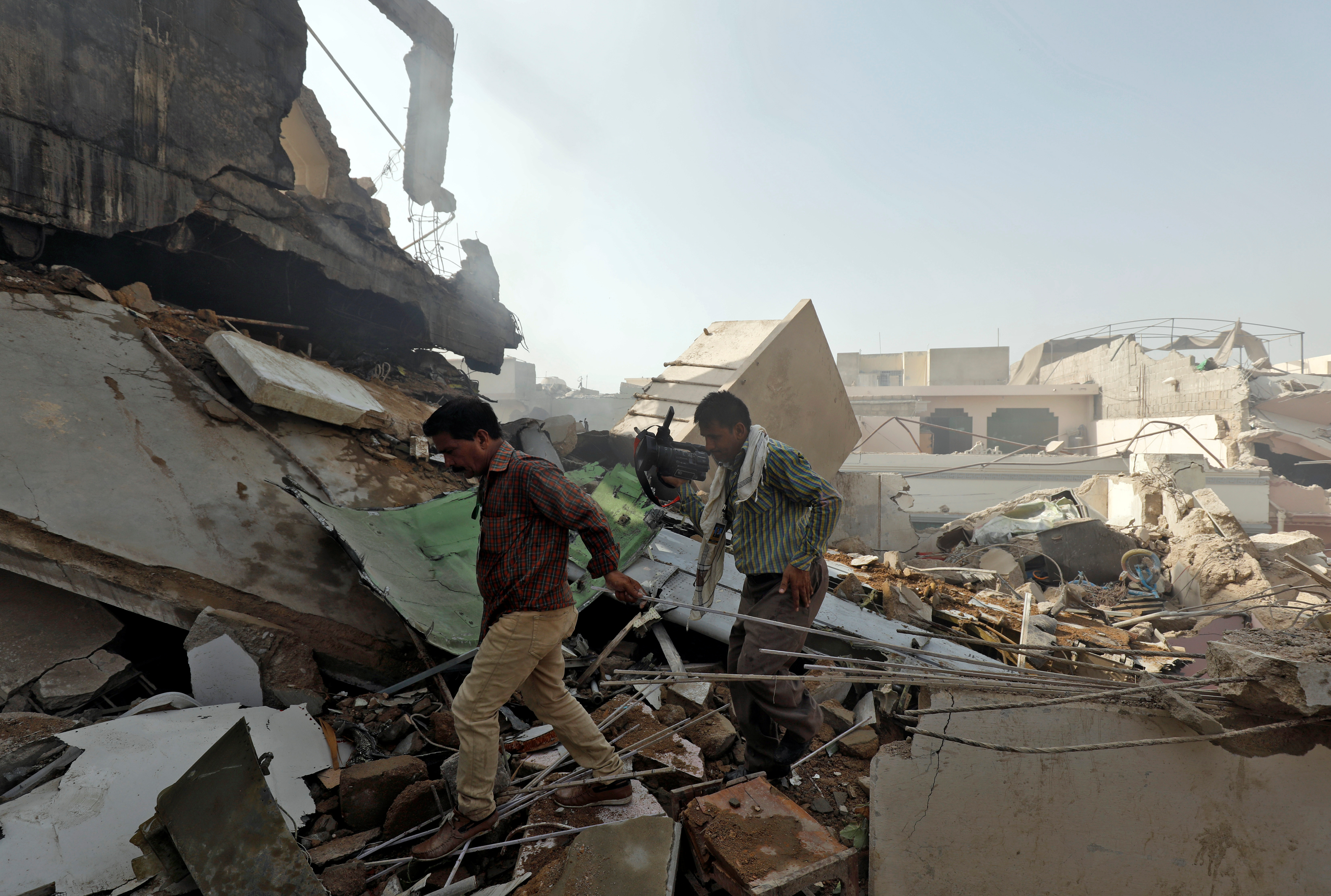 Men walk on the debris at the site of a passenger plane crash in a residential area near an airport in Karachi, Pakistan May 22, 2020. REUTERS/Akhtar Soomro - RC2OTG9SHZGA