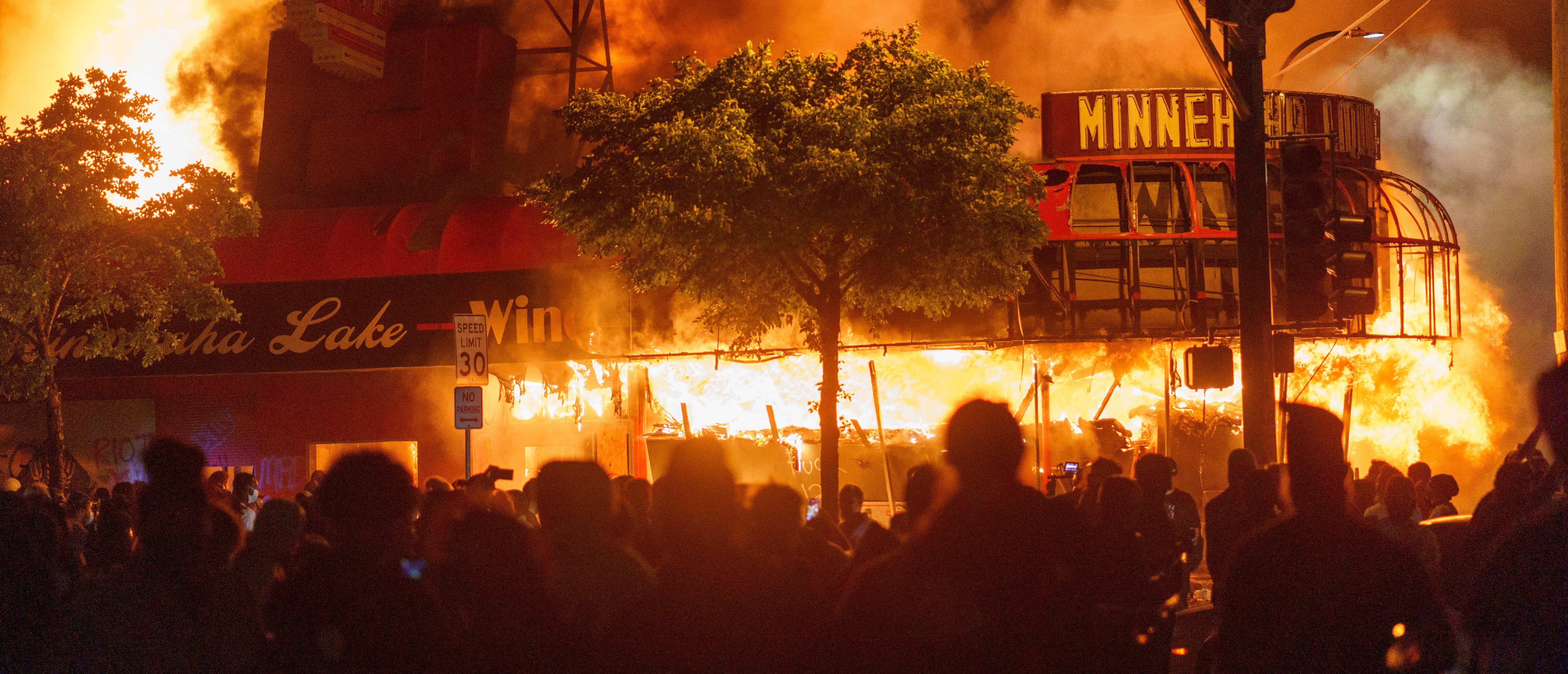 TOPSHOT - Protesters gather in front of a liquor store in flames near the Third Police Precinct on May 28, 2020 in Minneapolis, Minnesota, during a protest over the death of George Floyd, an unarmed black man, who died after a police officer kneeled on his neck for several minutes. - A police precinct in Minnesota went up in flames late on May 28 in a third day of demonstrations as the so-called Twin Cities of Minneapolis and St. Paul seethed over the shocking police killing of a handcuffed black man. The precinct, which police had abandoned, burned after a group of protesters pushed through barriers around the building, breaking windows and chanting slogans. A much larger crowd demonstrated as the building went up in flames. (Photo by kerem yucel / AFP) (Photo by KEREM YUCEL/AFP via Getty Images)