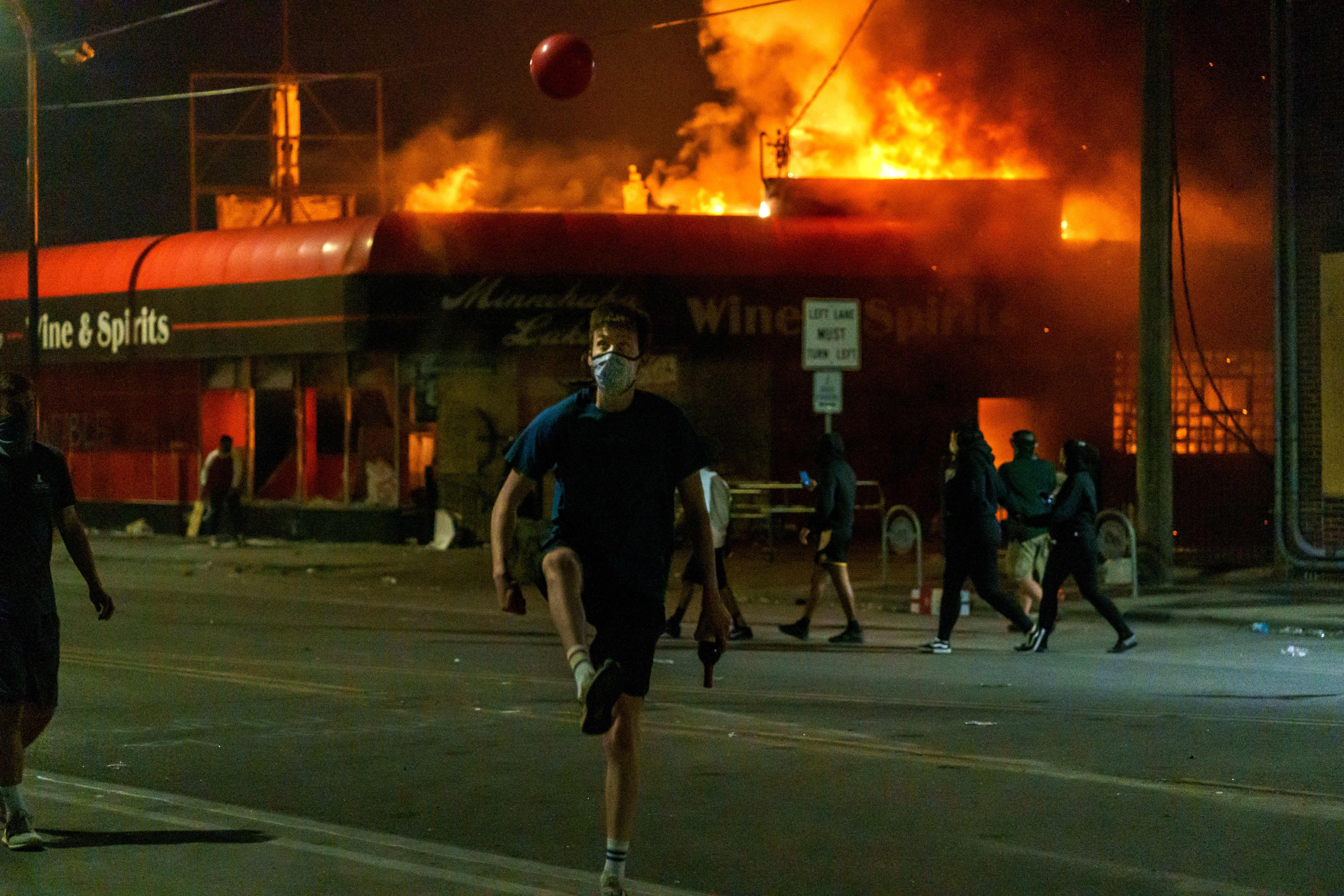A protester kicks a ball in front of a liquor store in flames on May 28, 2020 in Minneapolis, Minnesota, during a protest over the death of George Floyd, an unarmed black man, who died after a police officer kneeled on his neck for several minutes. (Photo by KEREM YUCEL/AFP via Getty Images)