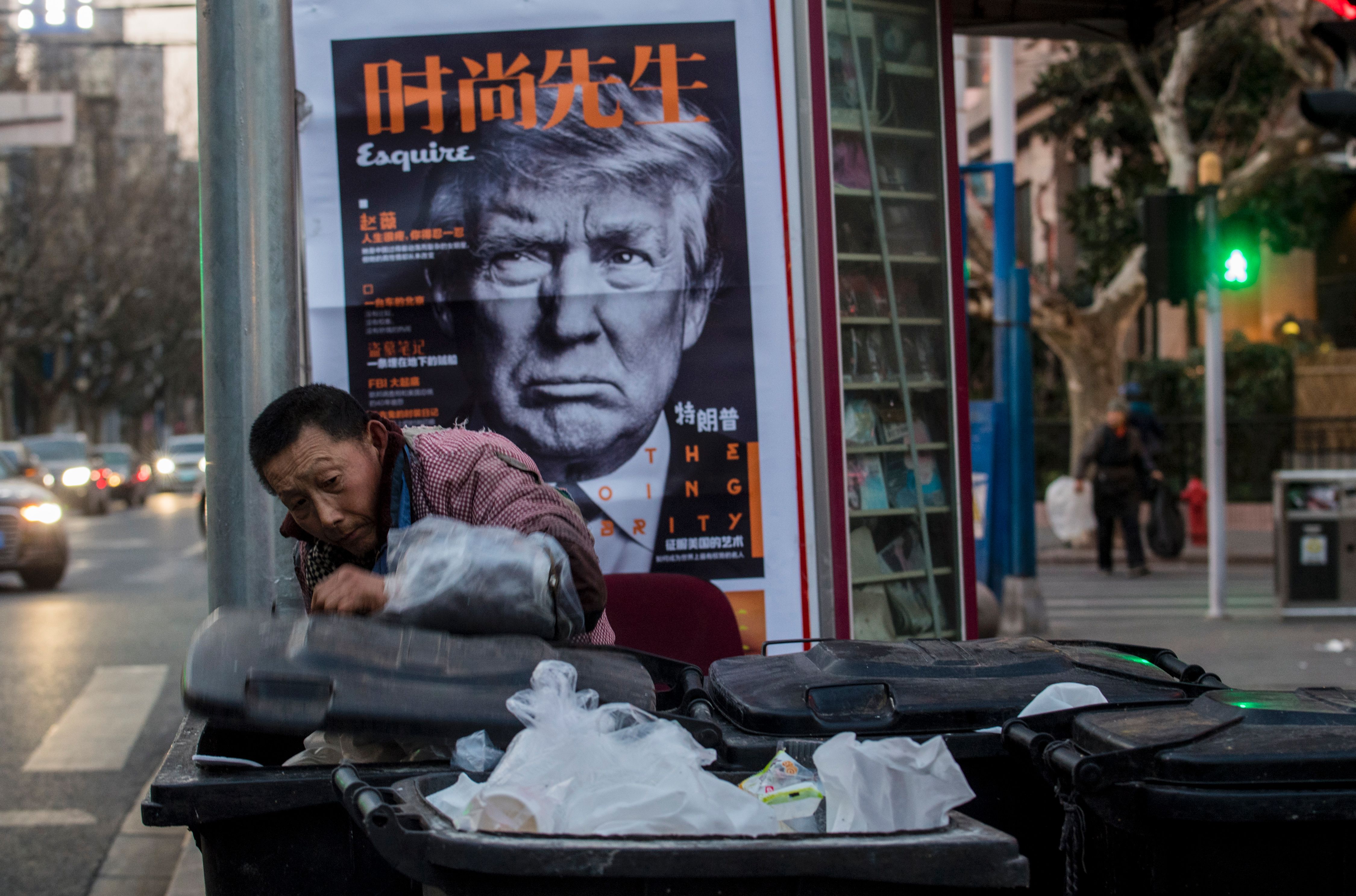 This picture taken on March 2, 2017 shows a man searching rubbish bins in front of an news stand advertising a Chinese newspaper with the front page photo of US President Donald Trump. / (JOHANNES EISELE/AFP via Getty Images)