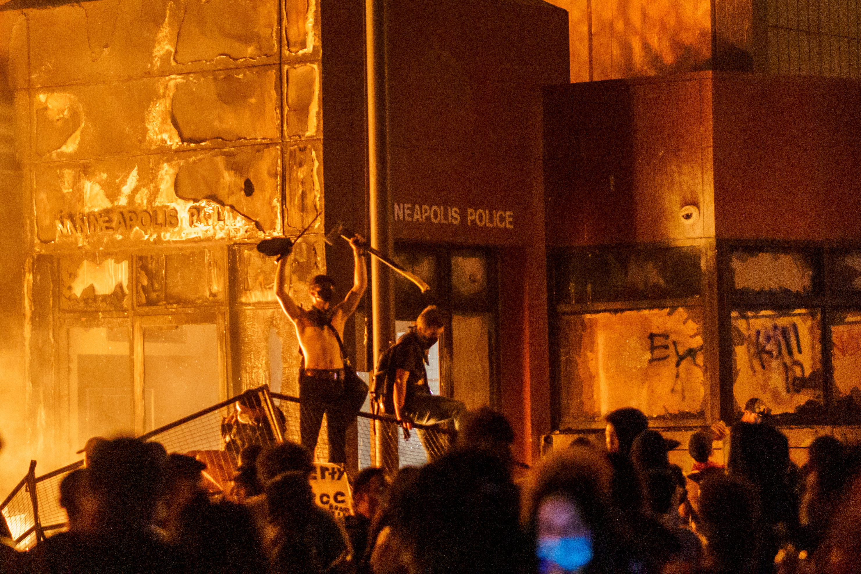 TOPSHOT - Flames from a nearby fire illuminate protesters standing on a barricade in front of the Third Police Precinct on May 28, 2020 in Minneapolis, Minnesota, during a protest over the death of George Floyd, an unarmed black man, who died after a police officer kneeled on his neck for several minutes. - A police precinct in Minnesota went up in flames late on May 28 in a third day of demonstrations as the so-called Twin Cities of Minneapolis and St. Paul seethed over the shocking police killing of a handcuffed black man. The precinct, which police had abandoned, burned after a group of protesters pushed through barriers around the building, breaking windows and chanting slogans. A much larger crowd demonstrated as the building went up in flames. (Photo by kerem yucel / AFP) (Photo by KEREM YUCEL/AFP via Getty Images)