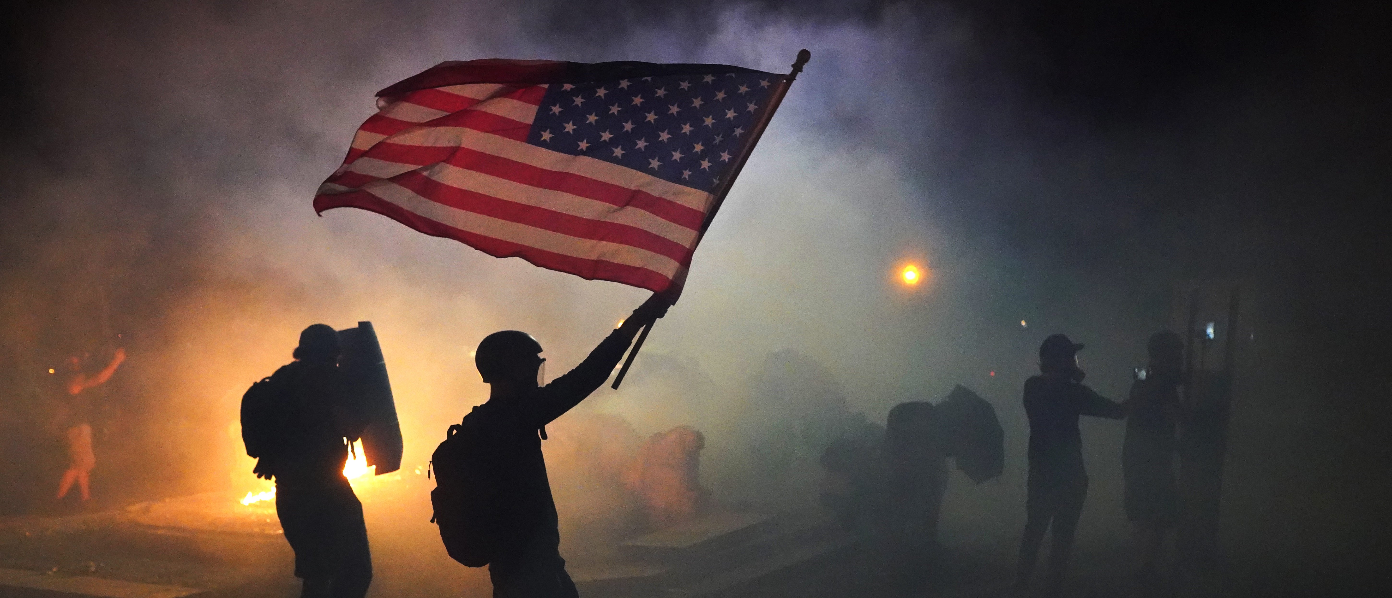 PORTLAND, OR - JULY 21: A protester flies an American flag while walking through tear gas fired by federal officers during a protest in front of the Mark O. Hatfield U.S. Courthouse on July 21, 2020 in Portland, Oregon. The federal police response to the ongoing protests against racial inequality has been criticized by city and state elected officials. (Photo by Nathan Howard/Getty Images)