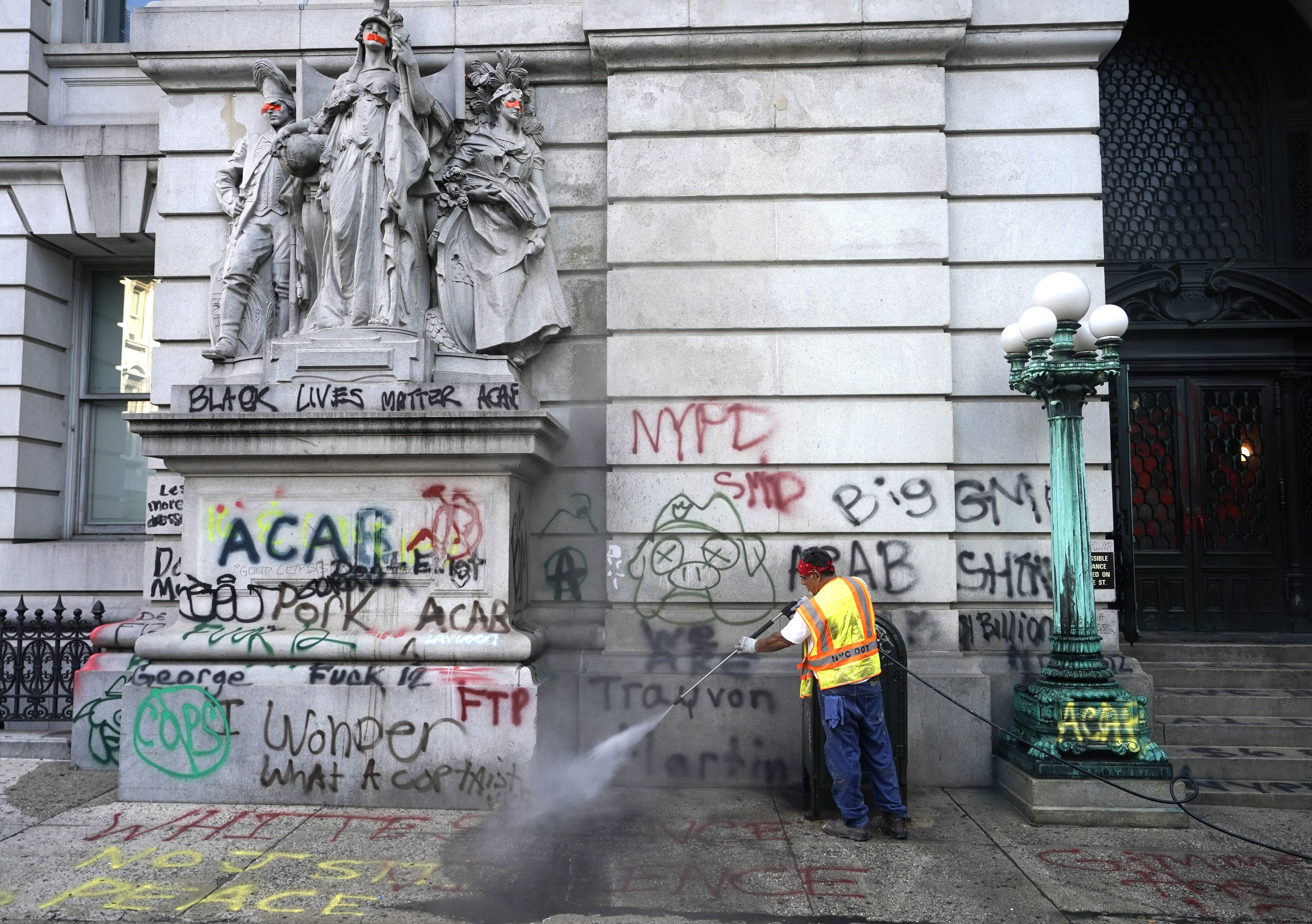 Sanitation workers clean up graffiti on July 22, 2020, after the Occupy City Hall protesters were cleared overnight by police - New York police removed the remaining Occupy City Hall protesters out of a month-long encampment. The protesters demanded a cut of at least $1 billion from the NYPD budget. The City Council approved the reform and Mayor Bill de Blasio signed into law. (Photo by TIMOTHY A. CLARY / AFP) (Photo by TIMOTHY A. CLARY/AFP via Getty Images)