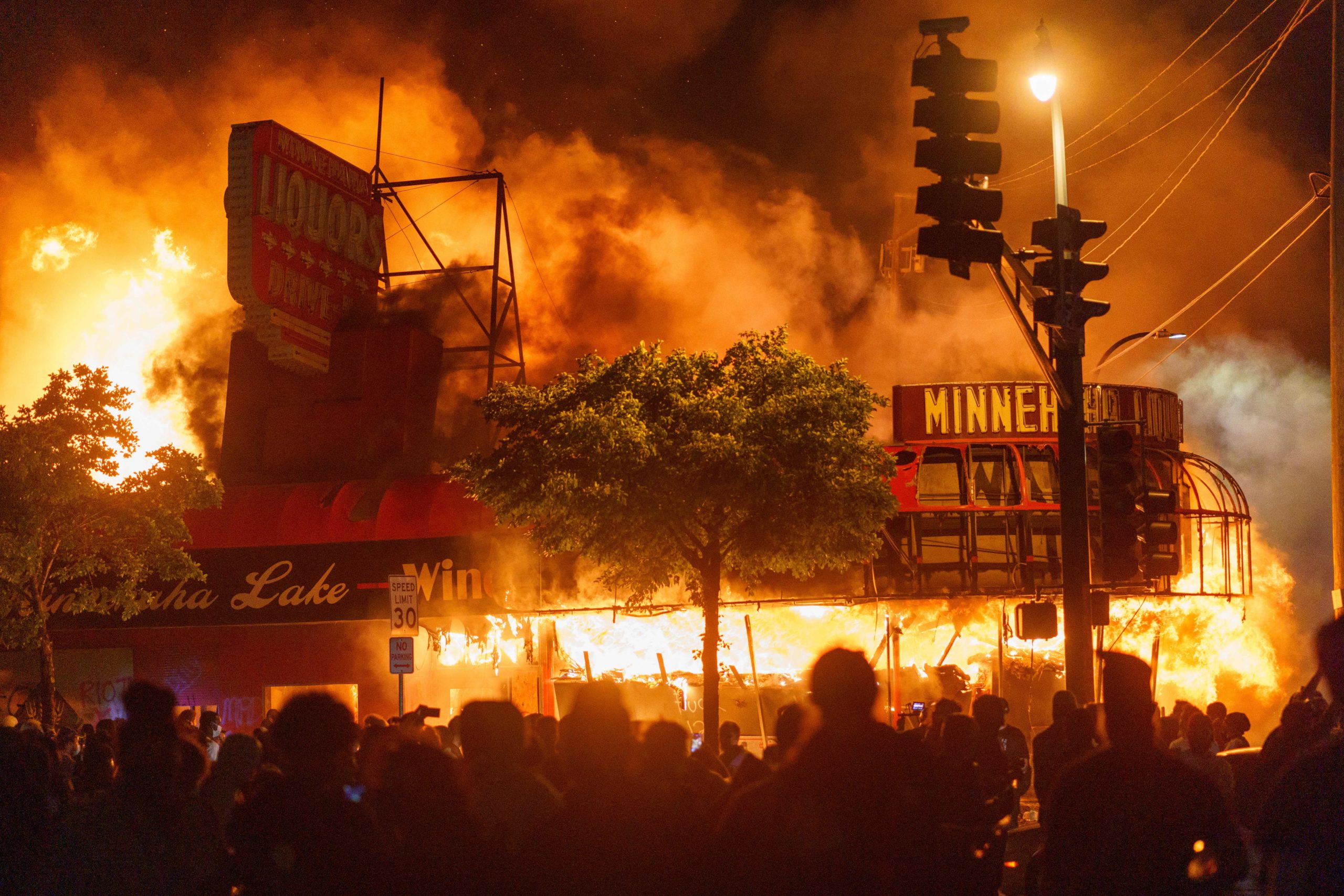TOPSHOT - Protesters gather in front of a liquor store in flames near the Third Police Precinct on May 28, 2020 in Minneapolis, Minnesota, during a protest over the death of George Floyd, an unarmed black man, who died after a police officer kneeled on his neck for several minutes. - A police precinct in Minnesota went up in flames late on May 28 in a third day of demonstrations as the so-called Twin Cities of Minneapolis and St. Paul seethed over the shocking police killing of a handcuffed black man. The precinct, which police had abandoned, burned after a group of protesters pushed through barriers around the building, breaking windows and chanting slogans. A much larger crowd demonstrated as the building went up in flames. (Photo by kerem yucel / AFP) (Photo by KEREM YUCEL/AFP via Getty Images)