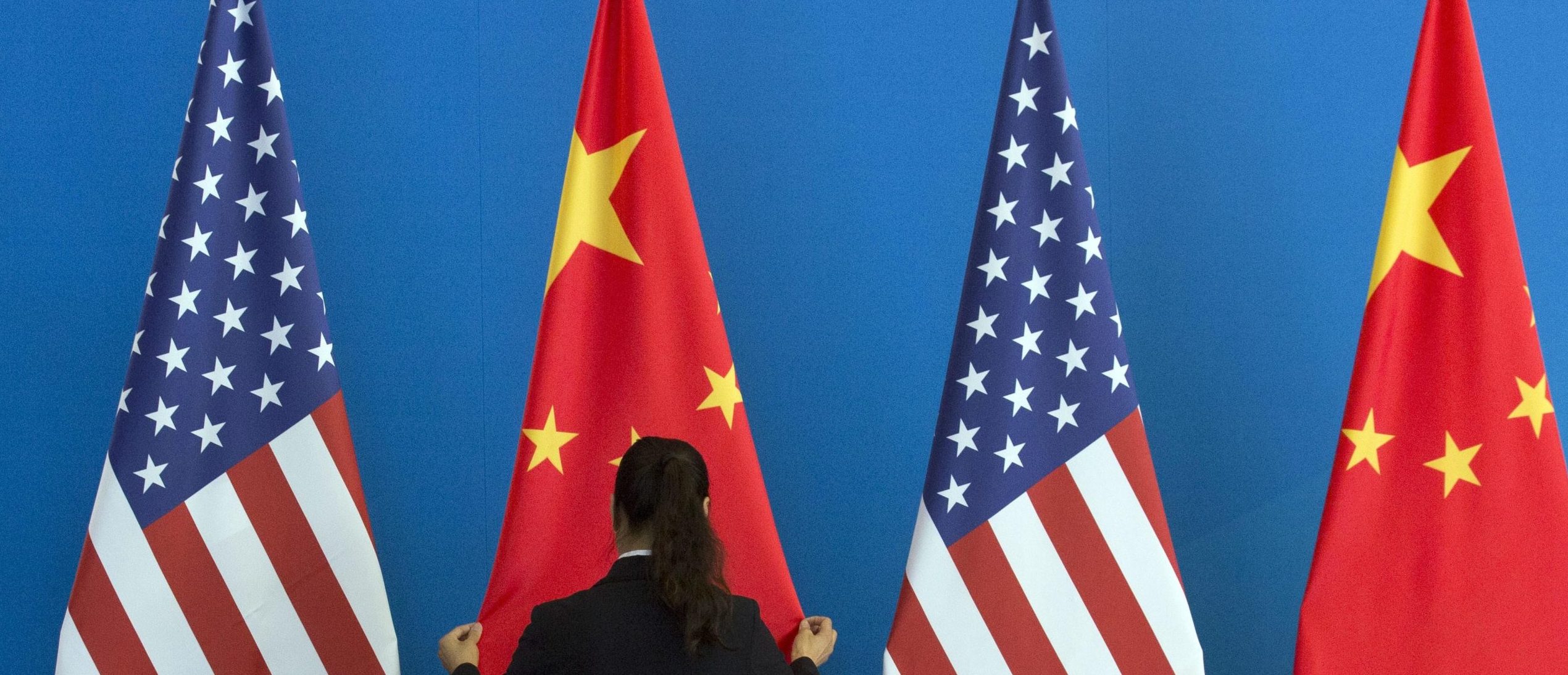 A Chinese woman adjusts a Chinese flag near US flags before the start of a Strategic Dialogue expanded meeting between China and the US during the US-China Strategic and Economic Dialogue held at the Diaoyutai State Guesthouse in Beijing on July 10, 2014. (NG HAN GUAN/AFP via Getty Images)