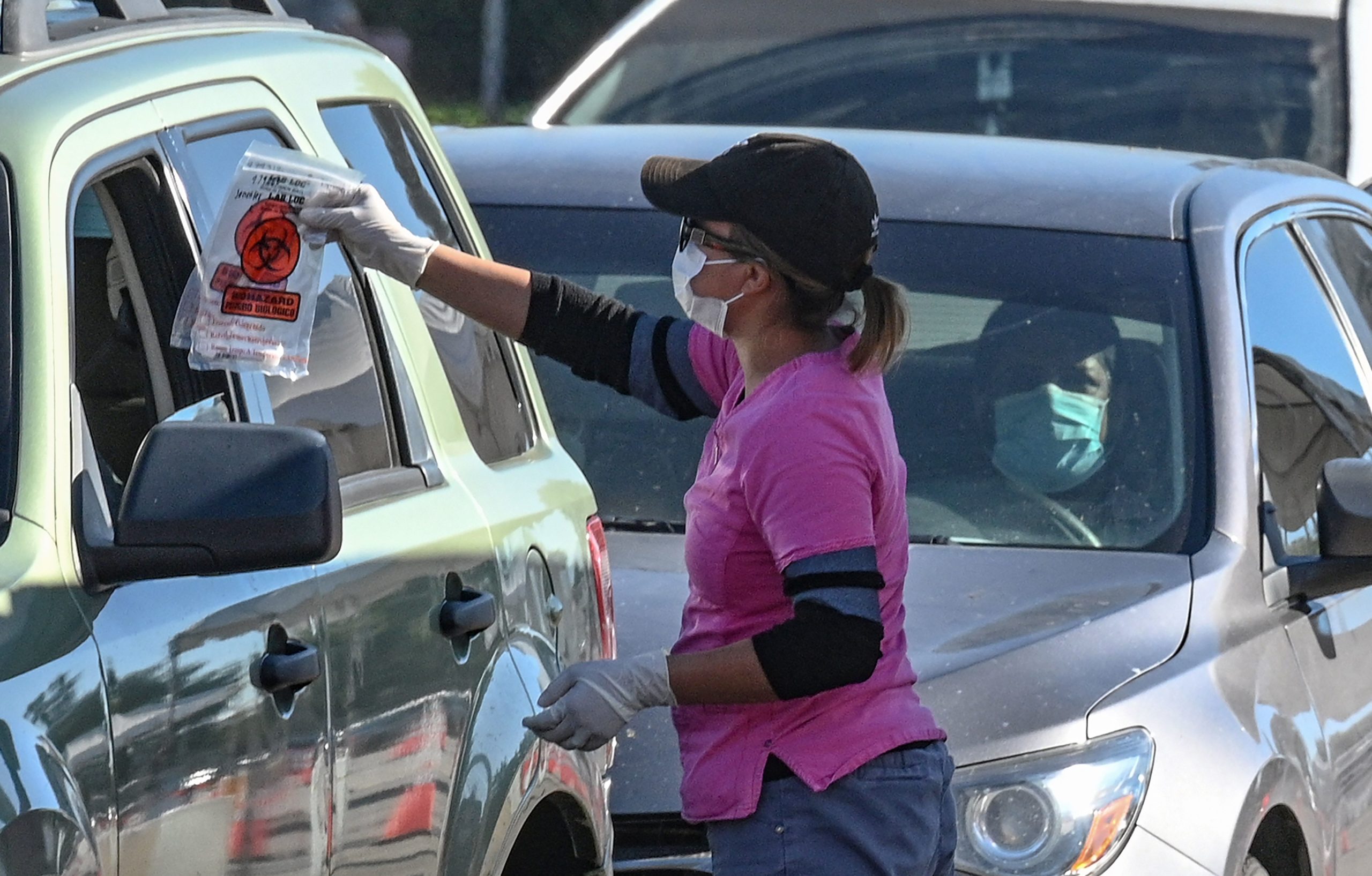 A coronavirus testing site staff member gives a self-administered test kit to a person in their car at a drive-up testing site in Los Angeles, California on Tuesday. (Robyn Beck/AFP via Getty Images)