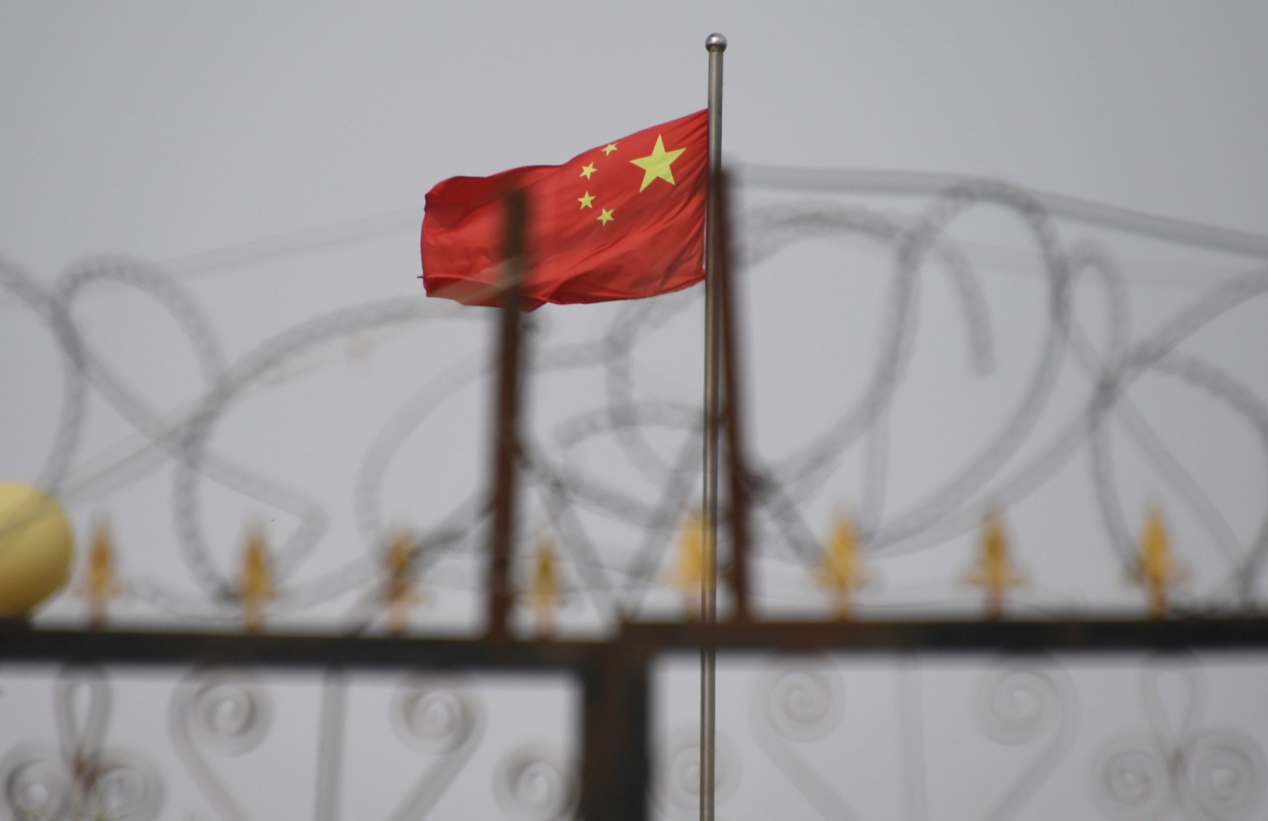 TOPSHOT - This photo taken on June 4, 2019 shows the Chinese flag behind razor wire at a housing compound in Yangisar, south of Kashgar, in China's western Xinjiang region. - A recurrence of the Urumqi riots which left nearly 200 people dead a decade ago is hard to imagine in today's Xinjiang, a Chinese region whose Uighur minority is straitjacketed by surveillance and mass detentions. A pervasive security apparatus has subdued the ethnic unrest that has long plagued the region. (Photo by GREG BAKER / AFP) (Photo by GREG BAKER/AFP via Getty Images)