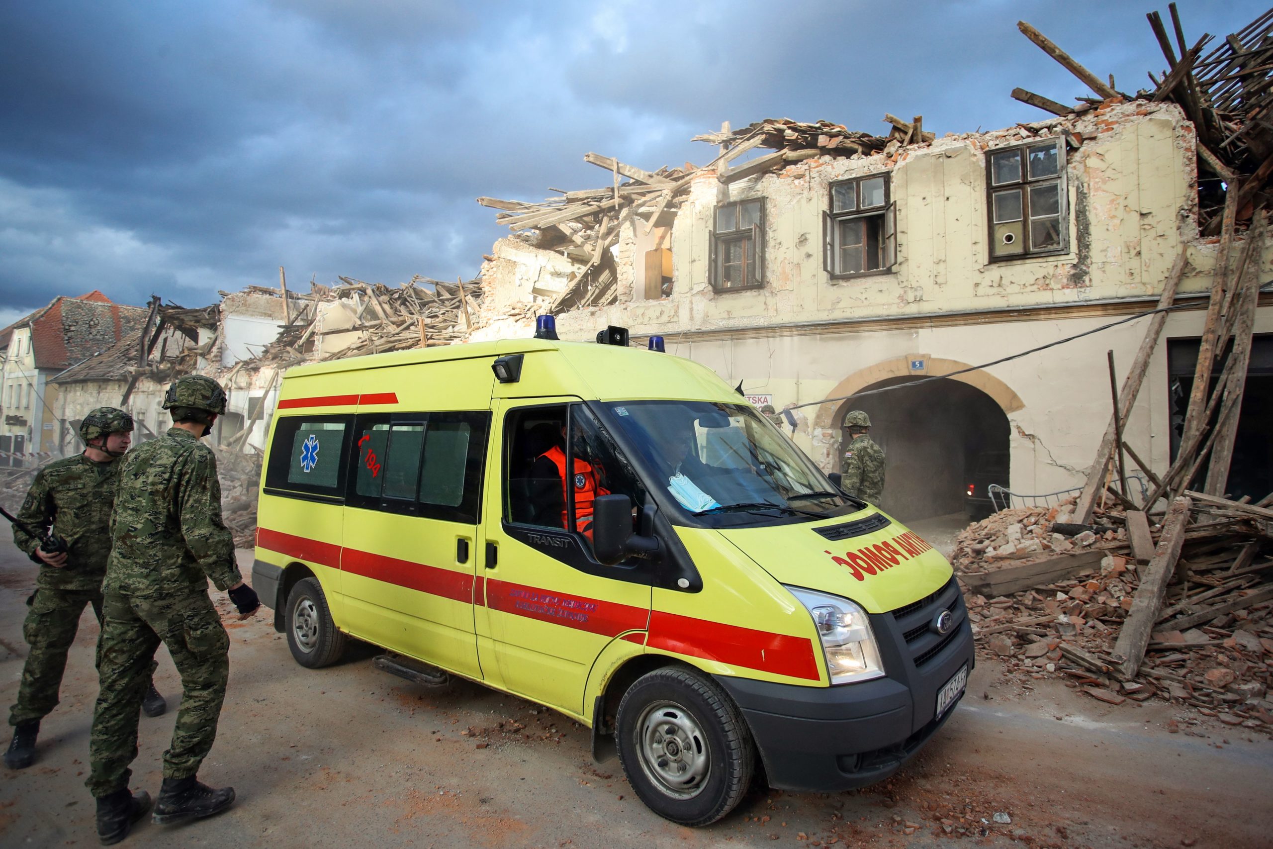 Crotian soldiers walk next to a first aid vehicle and damaged buildings in Petrinja, some 50kms from Zagreb, after the town was hit by an earthquake of the magnitude of 6,4 on December 29, 2020. - The tremor, one of the strongest to rock Croatia in recent years, collapsed rooftops in Petrinja, home to some 20,000 people, and left the streets strewn with bricks and other debris. Rescue workers and the army were deployed to search for trapped residents, as a girl was reported dead. (Photo by Damir Sencar/AFP via Getty Images)