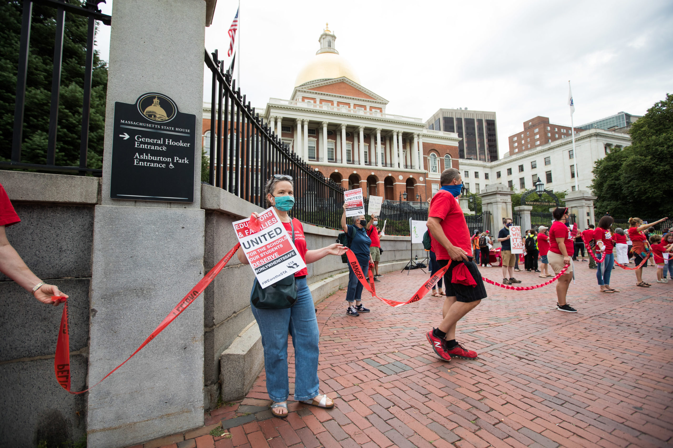 People participating in a protest organized by the American Federation of Teachers form a human chain around the Massachusetts State House on August 19, 2020 in Boston, Massachusetts. The group is calling for a uniform requirement for all districts to start the school year with a comprehensive distance learning plan (Photo by Scott Eisen/Getty Images)