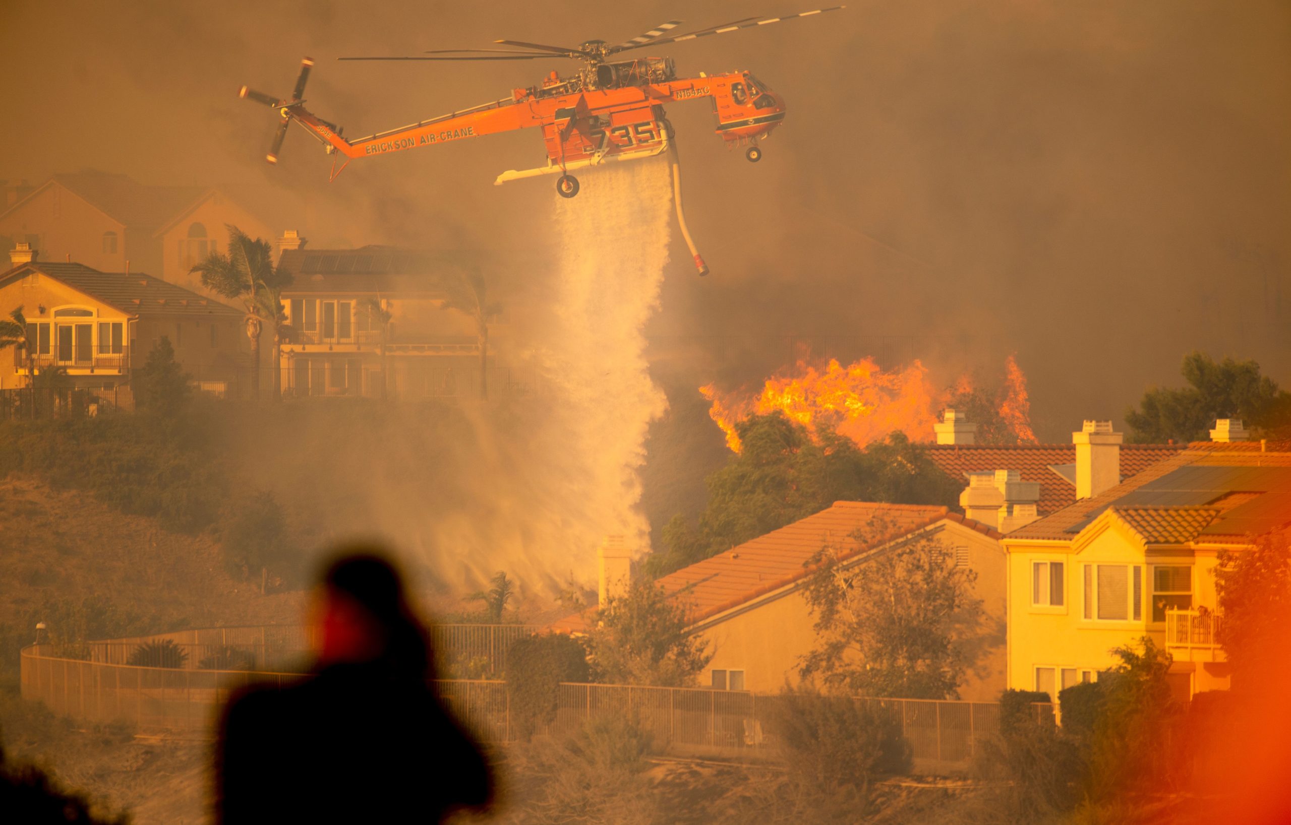 A helicopter drops water to help fight flames as the Saddleridge Fire in the Porter Ranch section of Los Angeles, California on October 11, 2019. - The fire broke out late October 10 and has scorched some 4,600 acres (1,816 hectares), and forced mandatory evacuation orders for 12,700 homes. (Photo by Josh Edelson / AFP) (Photo by JOSH EDELSON/AFP via Getty Images)