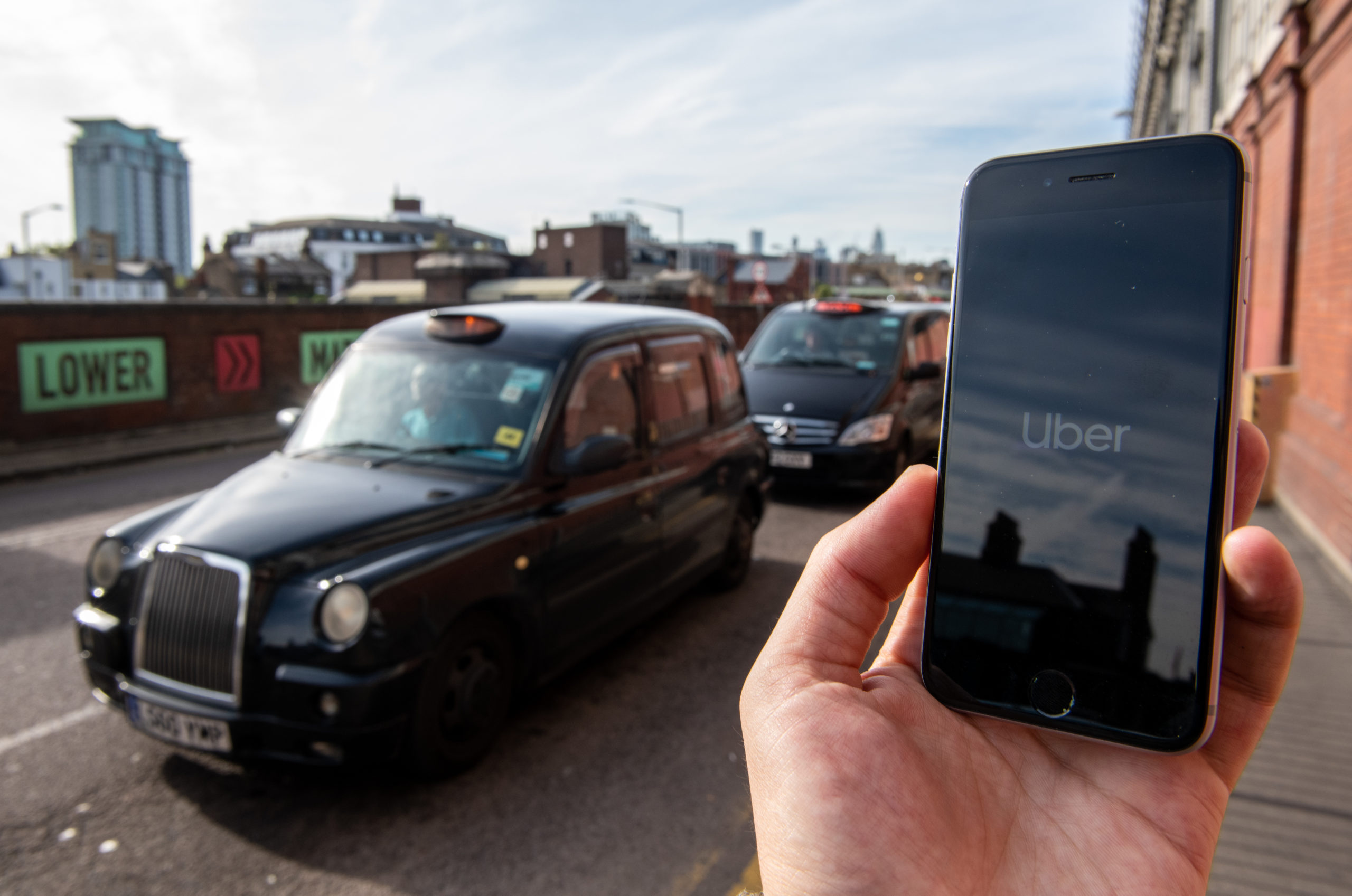 In this photo illustration a phone is held displaying the Uber logo in its app in front of a taxi stand in London, England. (Chris J Ratcliffe/Getty Images)