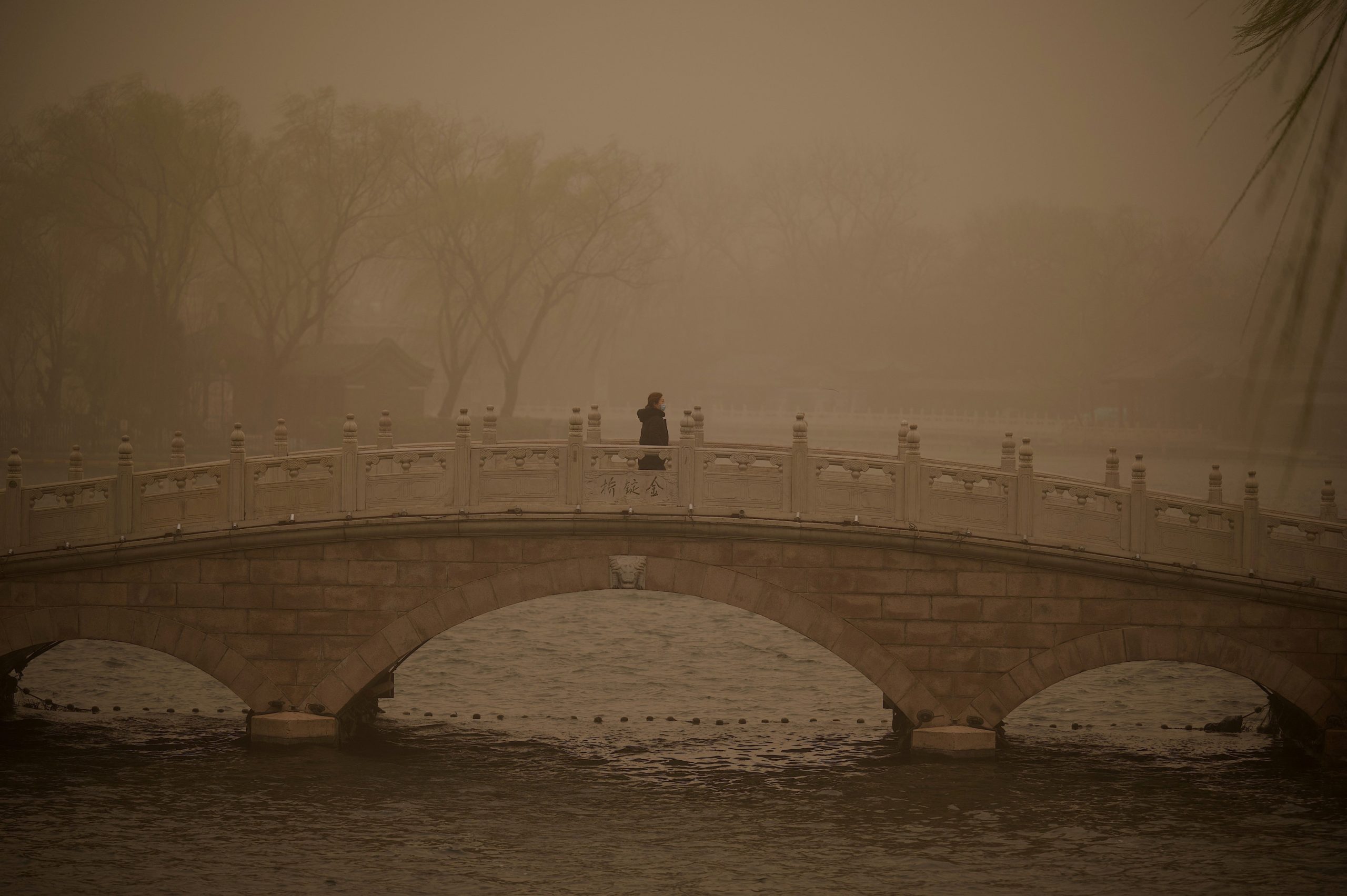 A woman crosses a bridge at Houhai lake during a sandstorm in Beijing on March 15, 2021. (Photo by Noel Celis / AFP) (Photo by NOEL CELIS/AFP via Getty Images)