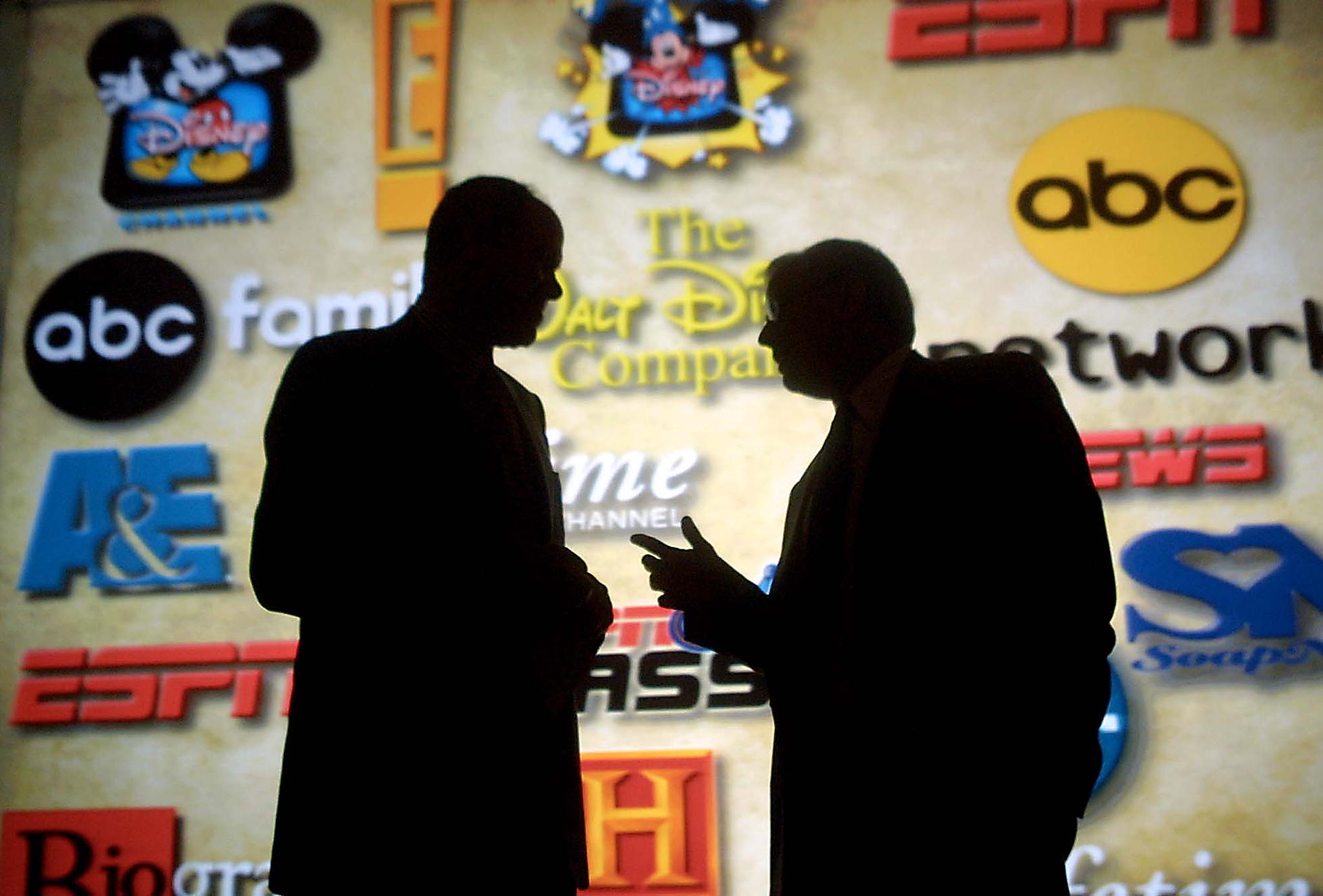 PASADENA, CA - JULY 23: Michael Eisner (L), chairman and CEO of the Walt Disney Company, talks with Mel Woods (R), president and CEO of the Haim Saban, in front of a projection, showing logos of the new acquisitions, during announcement of 100 percent purchase of Fox Family Worldwide and Haim Saban July 23, 2001 in Pasadena, CA. Fox Family and its subsidiaries will be renamed ABC Family. (Photo credit should read FREDERICK M. BROWN/AFP via Getty Images)