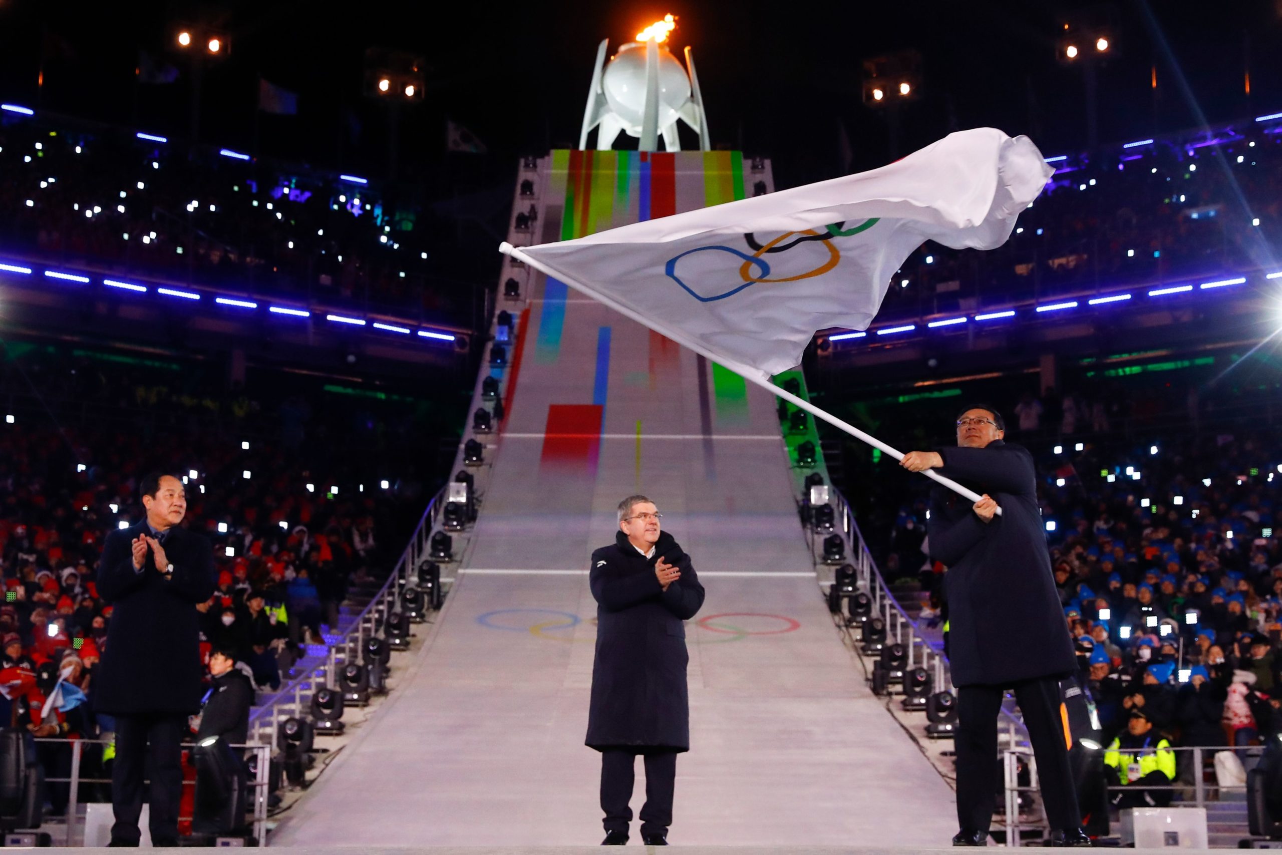 President of the International Olympic Committee Thomas Bach claps as the Mayor of Beijing Chen Jining waves the Olympic flag during the handover ceremony for the 2022 Beijing Winter Olympic Games. (Kai Pfaffenbach/Pool/AFP via Getty Images)