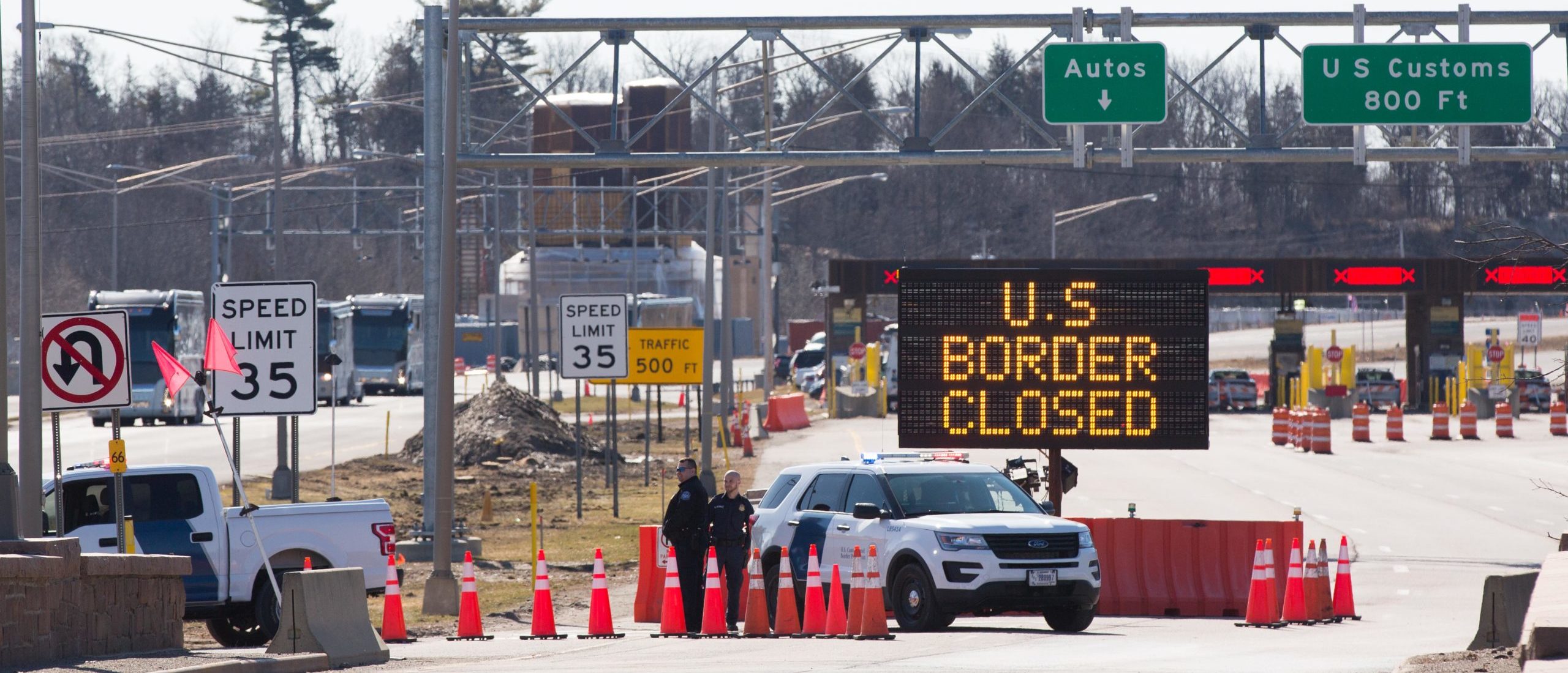 TOPSHOT - US Customs officers stand beside a sign saying that the US border is closed at the US/Canada border in Lansdowne, Ontario, on March 22, 2020. - The United States agreed with Mexico and Canada to restrict non-essential travel because of the coronavirus, COVID-19, outbreak and is planning to repatriate undocumented immigrants arriving from those countries. (Photo by Lars Hagberg / AFP) (Photo by LARS HAGBERG/AFP via Getty Images)