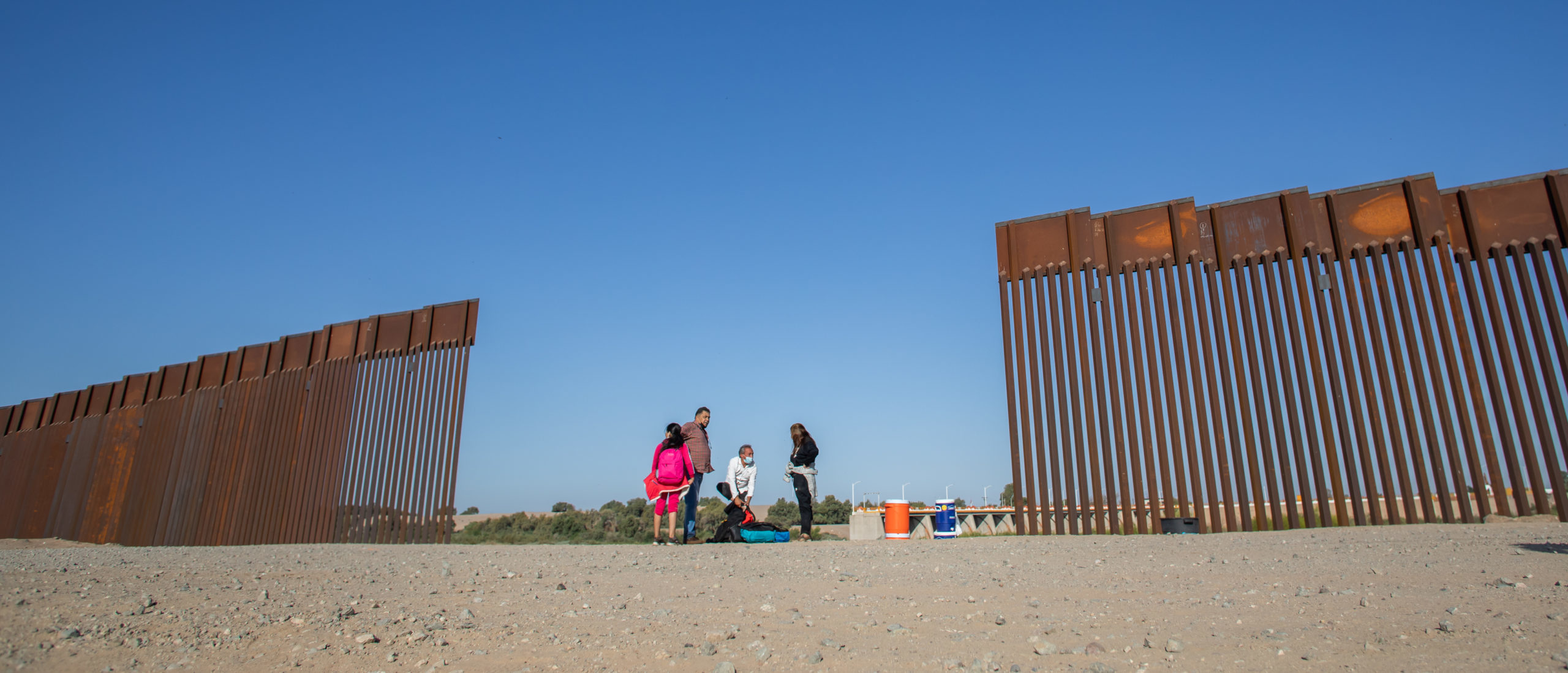 YUMA, AZ - MAY 13: A family of asylum seekers from Colombia walk through an opening in the wall at the US Mexico border to turn themselves in to US Border Patrol agents on May 13, 2021 in Yuma, Arizona. The Biden administration is trying to develop a plan to safely handle the surge of immigrants coming across the Southern border. (Photo by Apu Gomes/Getty Images)