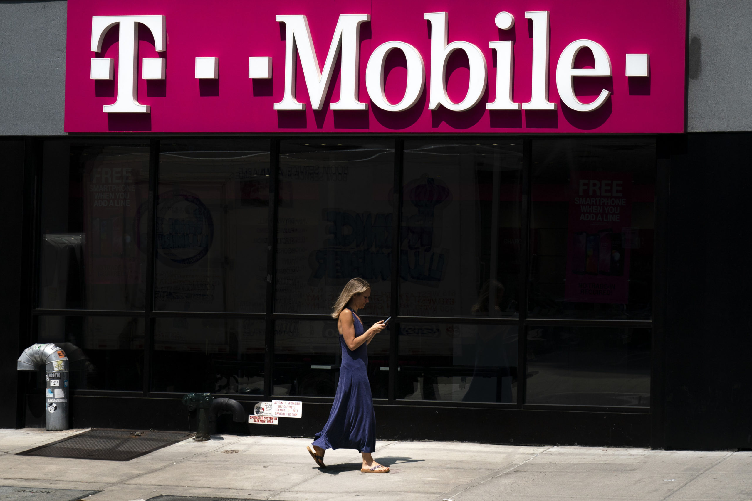 A woman looks on her phone as she walks past a T-Mobile store in New York City in 2019. (Drew Angerer/Getty Images)