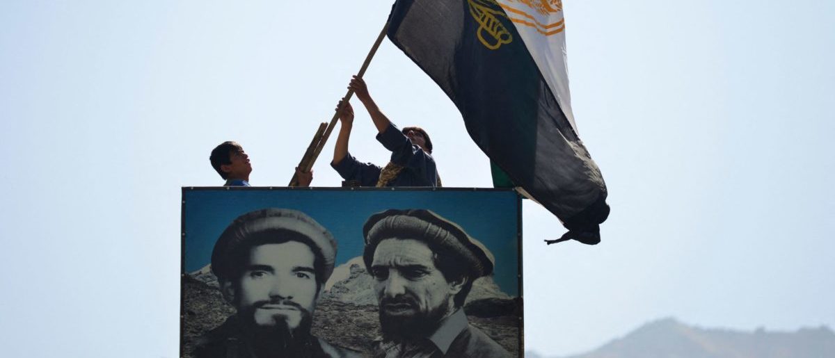 Afghan men wave a flag above the portrait of late Afghan commander Ahmad Shah Massoud (R) in Paryan district of Panjshir province on August 23, 2021, as the Taliban said their fighters had surrounded resistance forces holed up in the valley, but were looking to negotiate rather than take the fight to them. (Photo by Ahmad SAHEL ARMAN / AFP) (Photo by AHMAD SAHEL ARMAN/AFP via Getty Images)