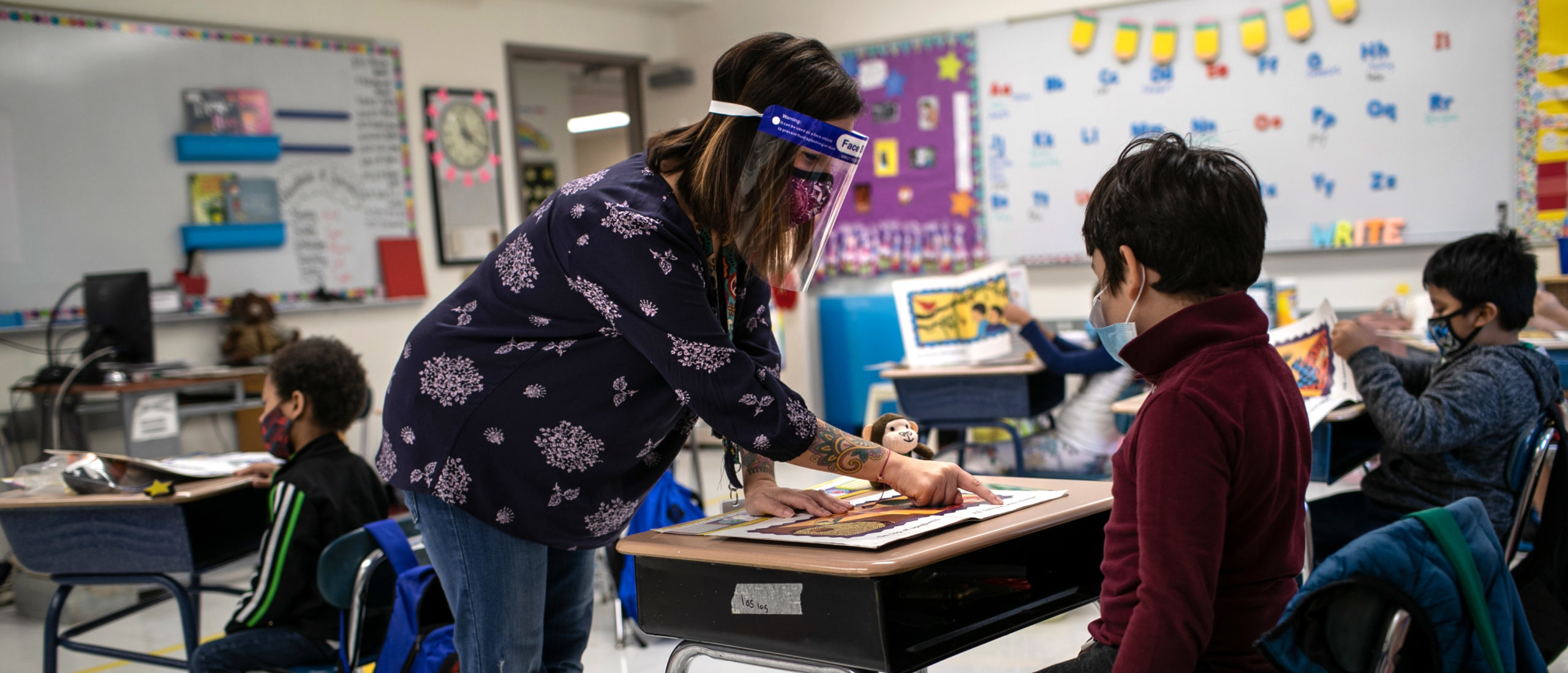 Teacher Elizabeth DeSantis, wearing a mask and face shield, helps a first grader during reading class at Stark Elementary School on September 16, 2020 in Stamford, Connecticut. (Photo by John Moore/Getty Images)