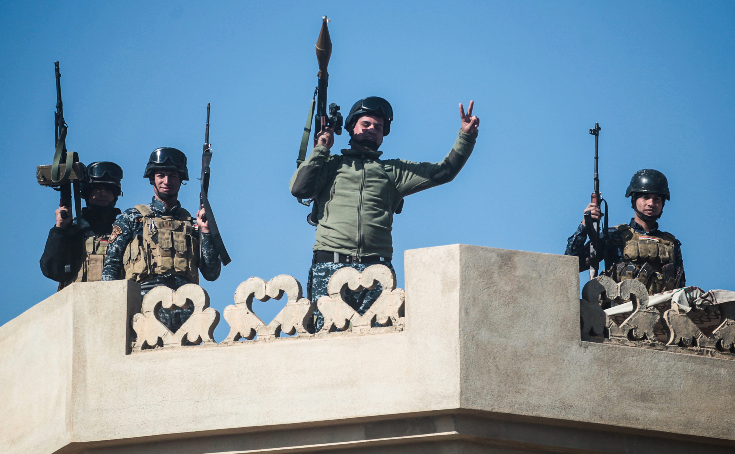 Members of the Iraqi security forces pose from atop a building, raising the victory gesture, in the village of al-Buseif, south of Mosul, during an offensive by Iraqi forces to retake the western side of the city from Islamic State (IS) group fighters on February 22, 2017. (AHMAD AL-RUBAYE/AFP via Getty Images)
