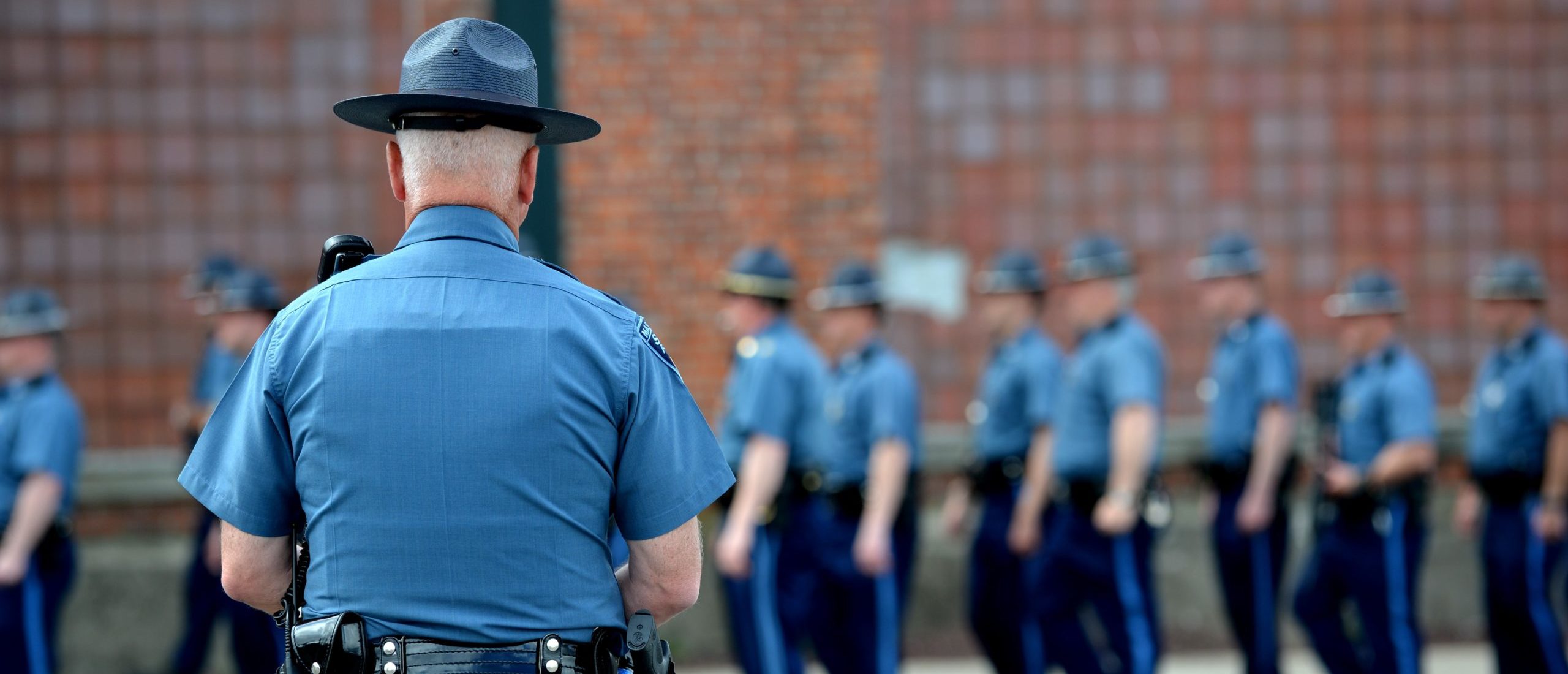A Massachusetts state trooper watches other troopers line up at the Watertown Mall as a search for the second of two suspects wanted in the Boston Marathon bombings takes place April 19, 2013 in Watertown, Massachusetts. Thousands of heavily armed police staged an intense manhunt Friday for a Chechen teenager suspected in the Boston marathon bombings with his brother, who was killed in a shootout. Dzhokhar Tsarnaev, 19, defied the massive force after his 26-year-old brother Tamerlan was shot and suffered critical injuries from explosives believed to have been strapped to his body. AFP PHOTO/Stan HONDA (Photo credit should read STAN HONDA/AFP via Getty Images)