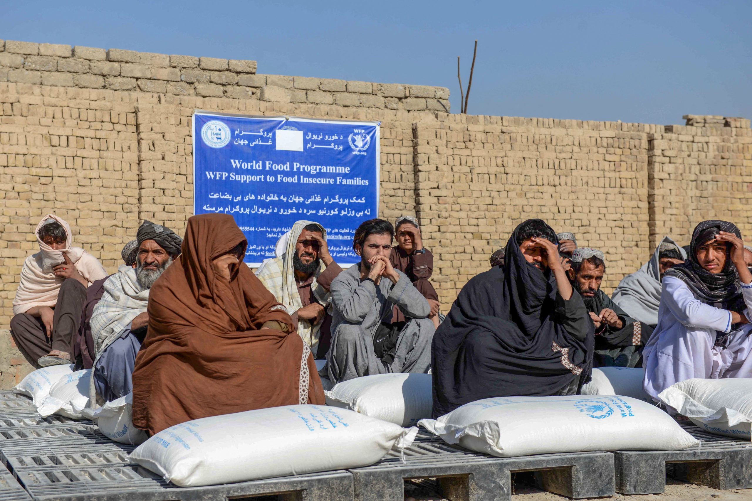 Afghan people sit besides sacks of food grains distributed as an aid by the World Food Programme (WFP) in Kandahar on October 19, 2021. (Photo by JAVED TANVEER/AFP via Getty Images)