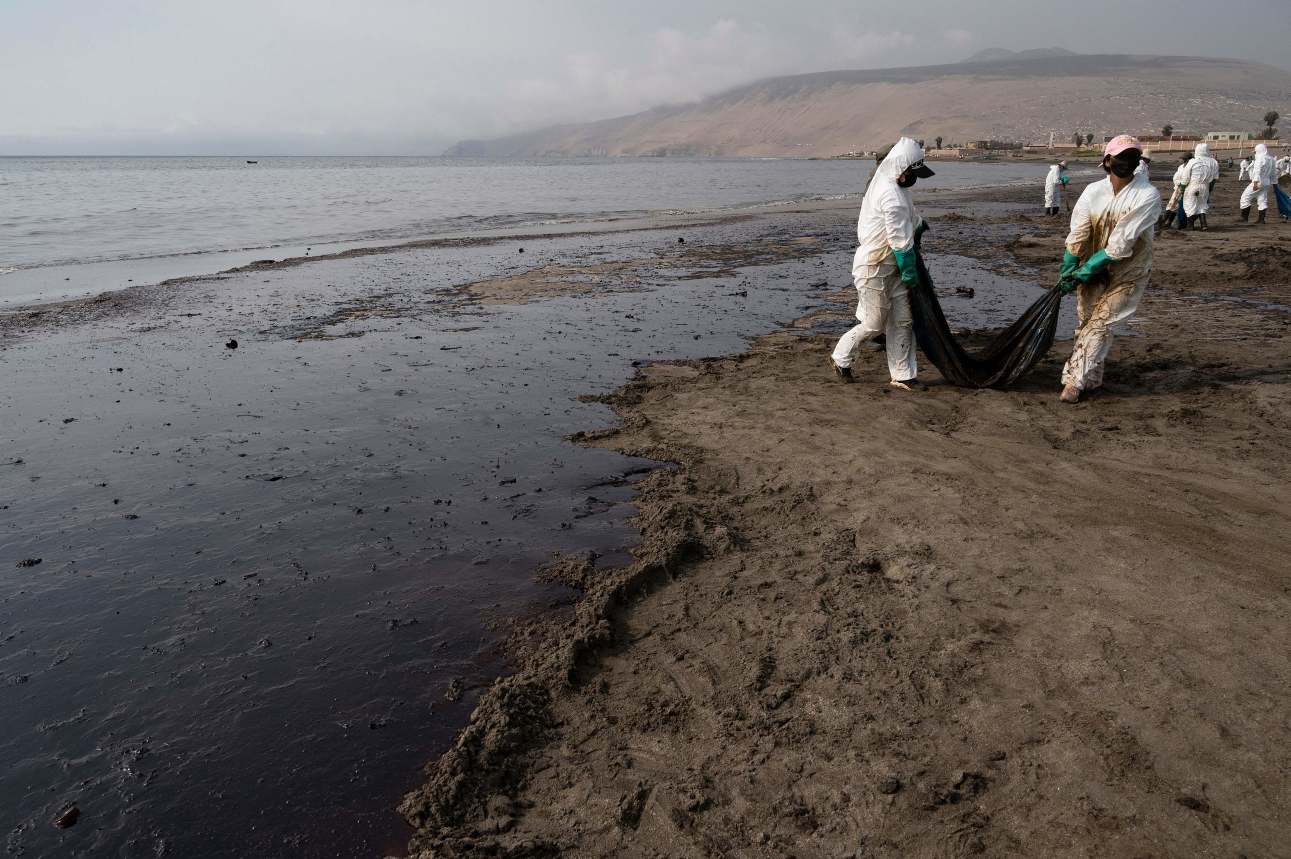 Cleaning crews work to remove oil from a beach annexed to the summer resort town of Ancon, northern Lima, on January 20, 2022 after a spill which occurred during the offloading process of the Italian-flagged tanker "Mare Doricum" at La Pampilla refinery caused by the abnormal waves recorded after the volcanic eruption in Tonga. (Photo by CRIS BOURONCLE/AFP via Getty Images)