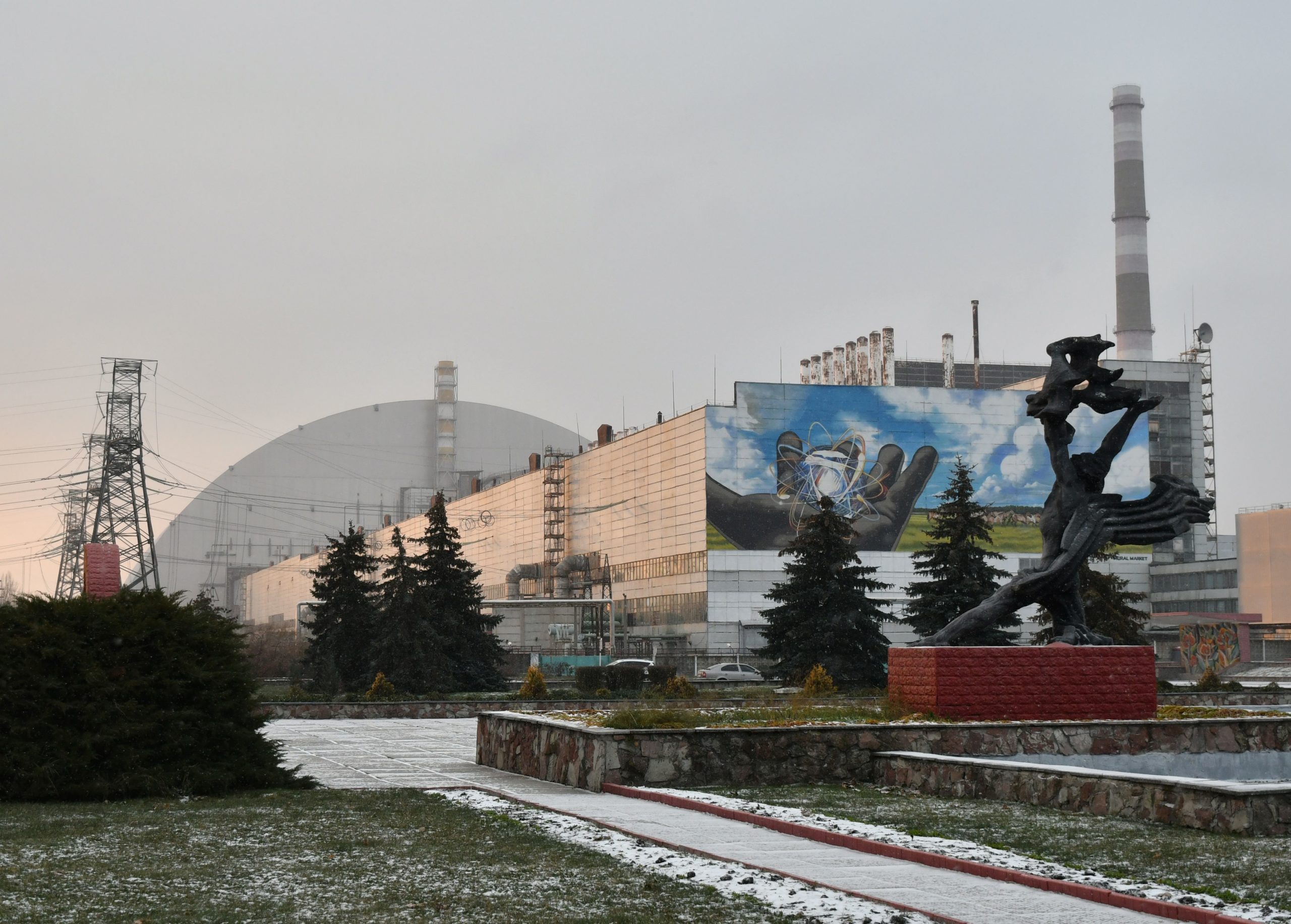 This photograph taken on December 8, 2020 shows a monument in front of the giant protective dome built over the sarcophagus of the destroyed fourth reactor of Chernobyl nuclear power plant. - More than three decades after the Chernobyl nuclear disaster forced thousands to evacuate, there is an influx of visitors to the area that has spurred officials to seek official status from UNESCO. Officials hope recognition from the UN's culture agency will boost the site as a tourist attraction and in turn bolster efforts to preserve ageing buildings nearby. (Photo by GENYA SAVILOV / AFP) (Photo by GENYA SAVILOV/AFP via Getty Images)