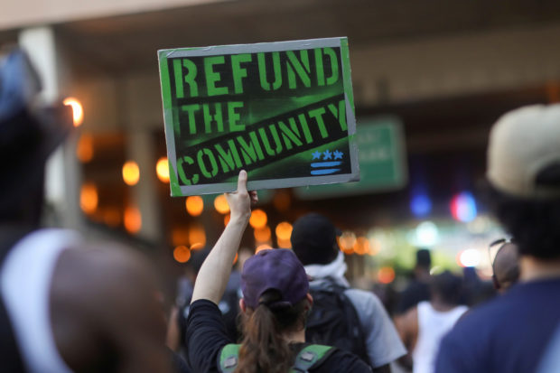 A protester holds up a "Refund the community" placard as he joins others marching into a traffic tunnel leading to a highway during racial inequality protests in Washington, U.S., June 23, 2020. REUTERS/Leah Millis