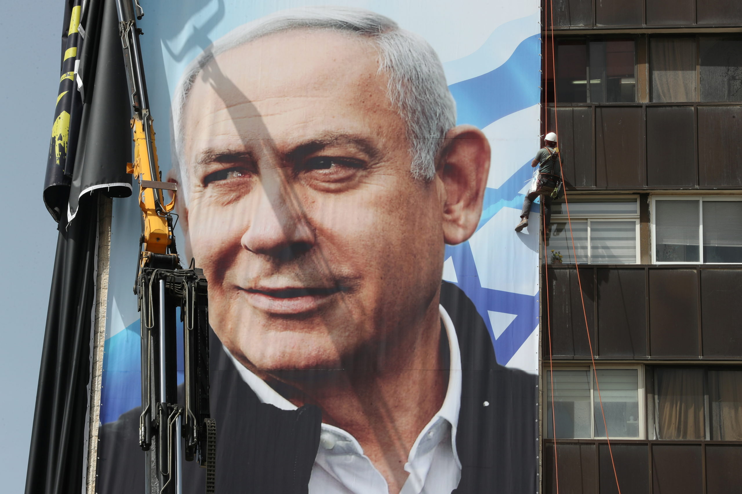 A worker hangs a Likud party election campaign banner depicting Israeli Prime Minister Benjamin Netanyahu's party leader, ahead of a March 23 vote, in Jerusalem on March 10, 2021. 