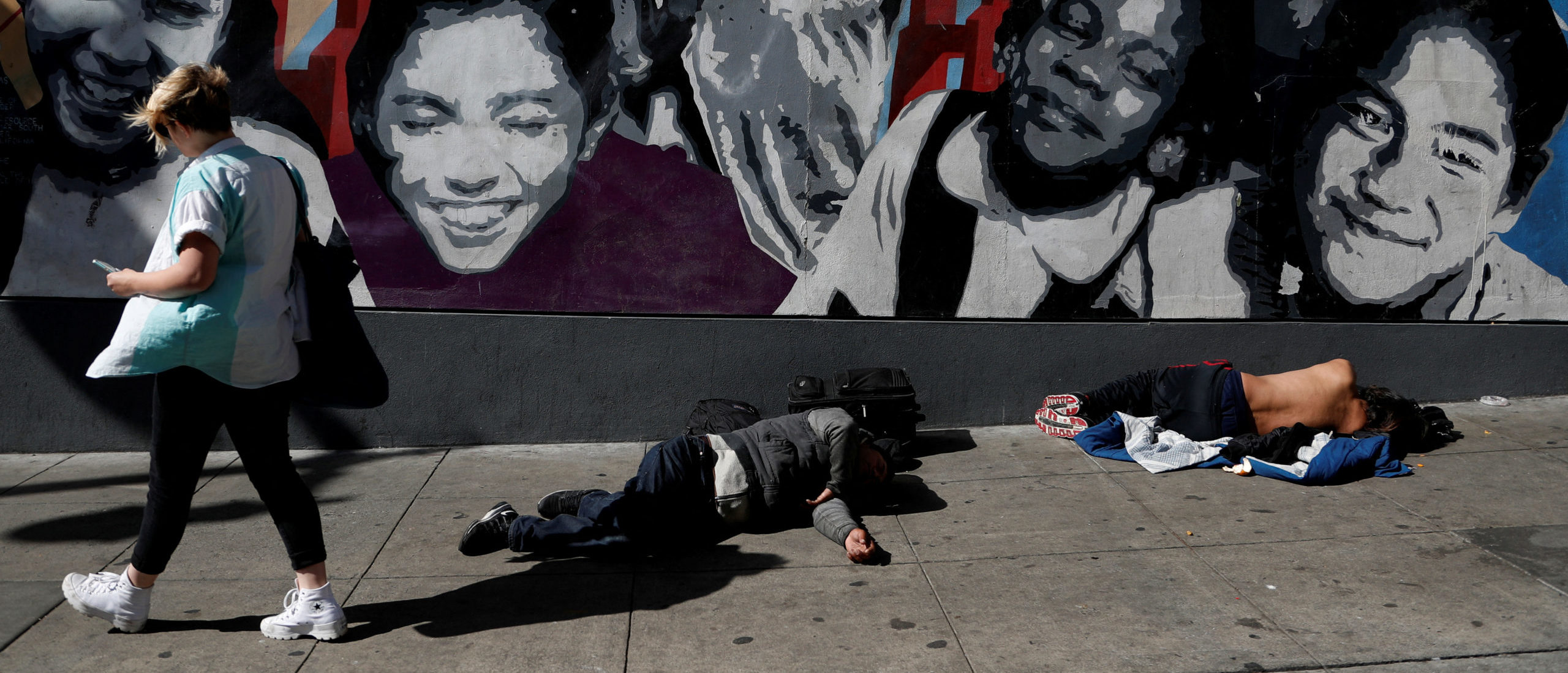 A woman walks past men passed out on the sidewalk n the Tenderloin area of San Francisco, California, U.S., February 28, 2020. Picture taken February 28, 2020. REUTERS/Shannon Stapleton/File Photo