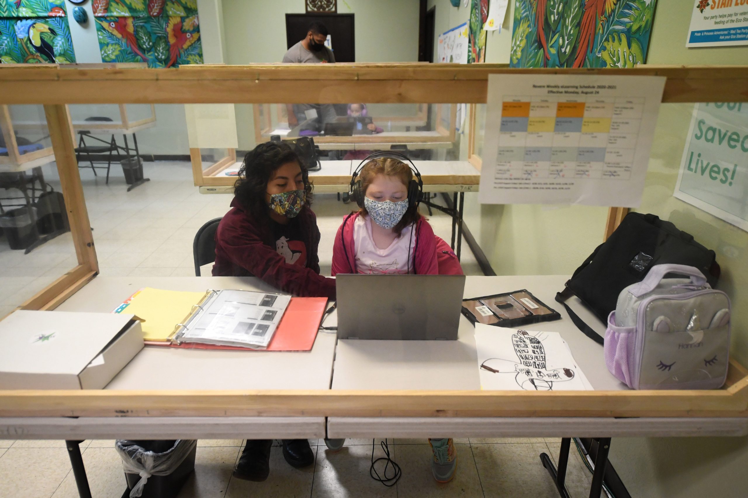 An instructor (L) helps a student with her online school lesson at a desk separated from others by plastic barriers at STAR Eco Station Tutoring & Enrichment Center on September 10, 2020 in Culver City, California. - California public school students will continue to learn at home, in private learning pods, or at specialized enrichment centers like Star Eco Station as the coronavirus pandemic continues, after a lawsuit brought by the Orange County Board of Education seeking to compel the state to reopen public schools was shot down by the California Supreme Court on September 10. (Photo by Robyn Beck / AFP) (Photo by ROBYN BECK/AFP via Getty Images)