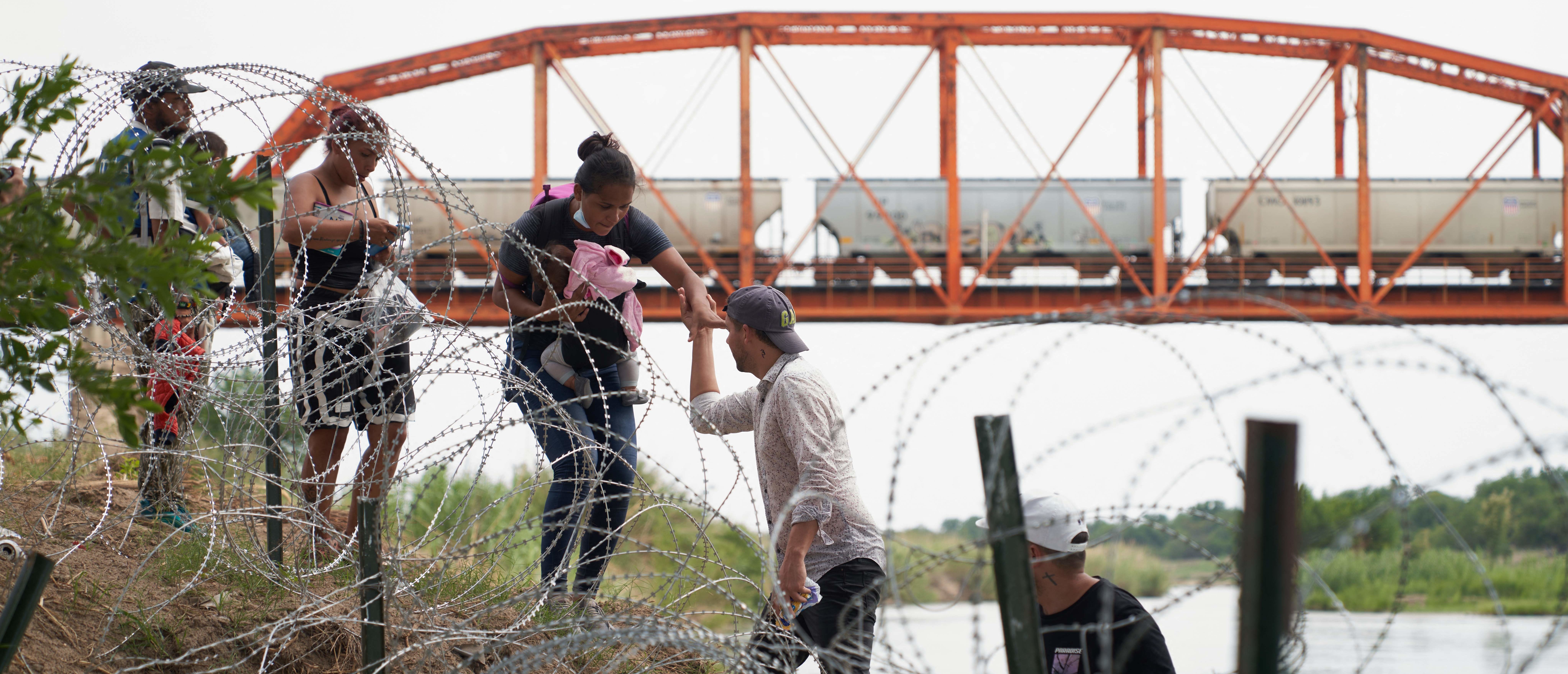 Migrants who illegally crossed the Rio Grande River walk along concertina wire in Eagle Pass, Texas, on May 22, 2022. - A Louisiana federal judge blocked the Biden administration on Friday from ending Title 42, a pandemic-related border restriction that allows for the immediate expulsion of asylum-seekers and other migrants. (Photo by allison dinner / AFP) (Photo by ALLISON DINNER/AFP via Getty Images)