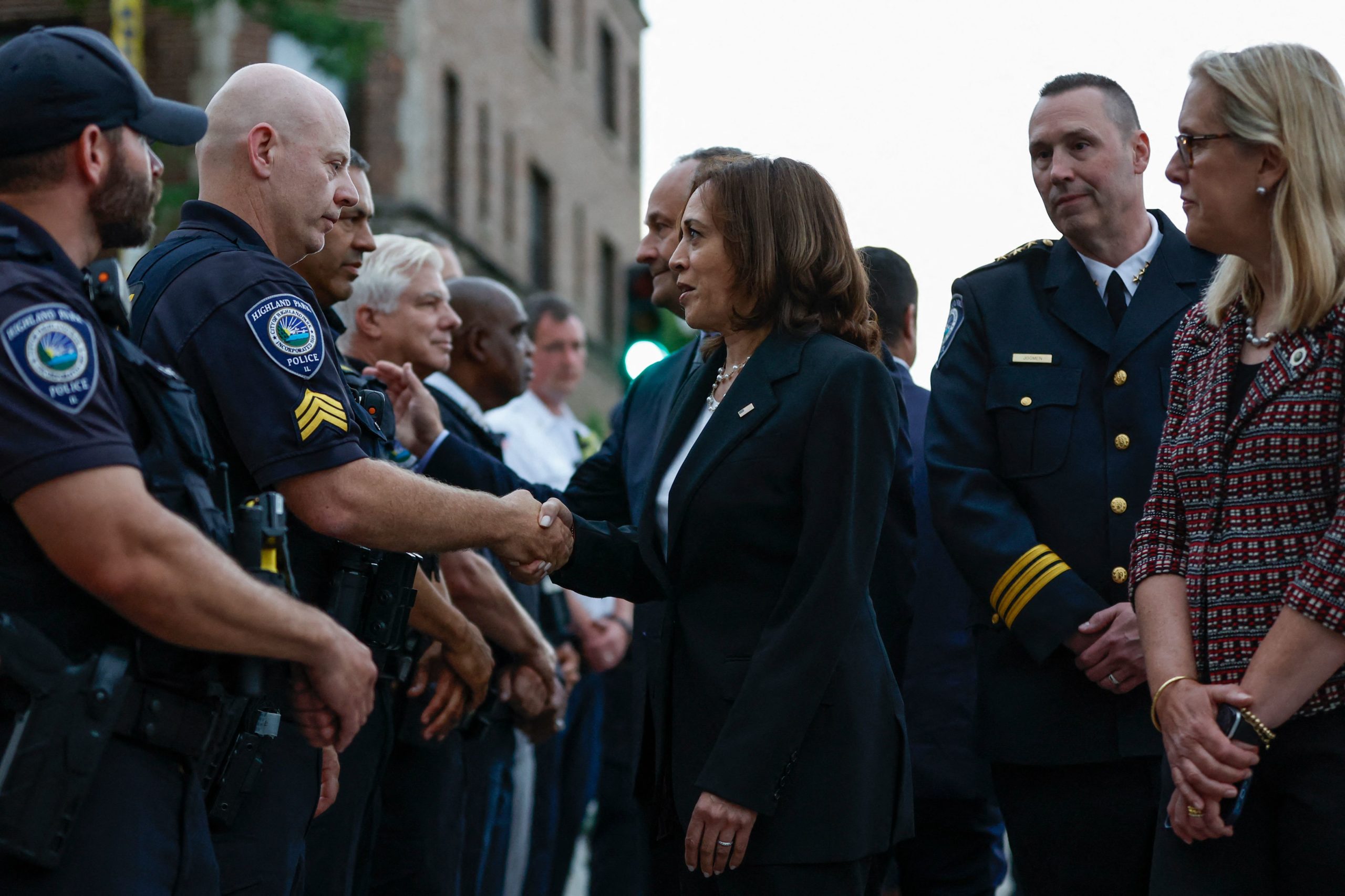 US Vice President Kamala Harris accompanied by Second Gentleman Doug Emhoff and Highland Park Mayor Nancy Rotering (R), talks with police officers during a surprise visit to the site of a shooting that left seven people dead in Highland Park, Illinois, on July 5, 2022. (Photo by KAMIL KRZACZYNSKI/AFP via Getty Images)