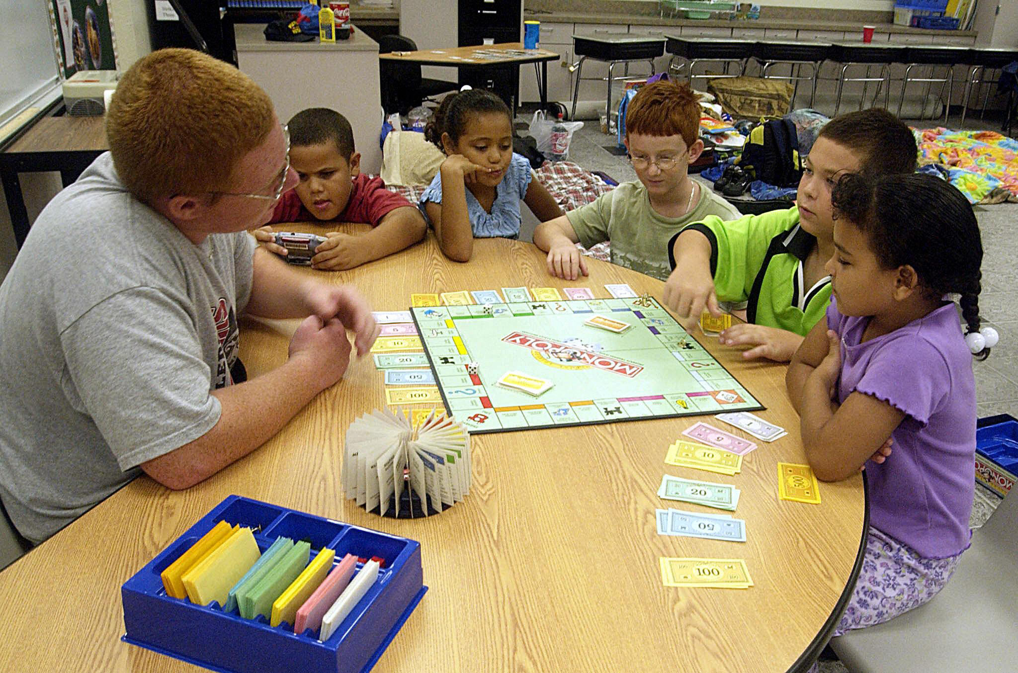 Robby Herto (L) helps the younger children (L-R) Tyler Leblant, Tiara McKelvin, Zackary Herto, Alex Leblant and Michaela McKelvin pass time with a game of Monopoly 04 September, 2004, in a classroom at Manatee elementary school near Melbourne, Florida. The school was opened as an emergency shelter and quickley filled to over 800 people in advance of approaching catagory 2 Hurricane Frances that is predicted to make landfall near Fort Pierce along Florida's East Central coast Saturday. AFP PHOTO/ Bruce WEAVER (Photo credit should read BRUCE WEAVER/AFP via Getty Images)