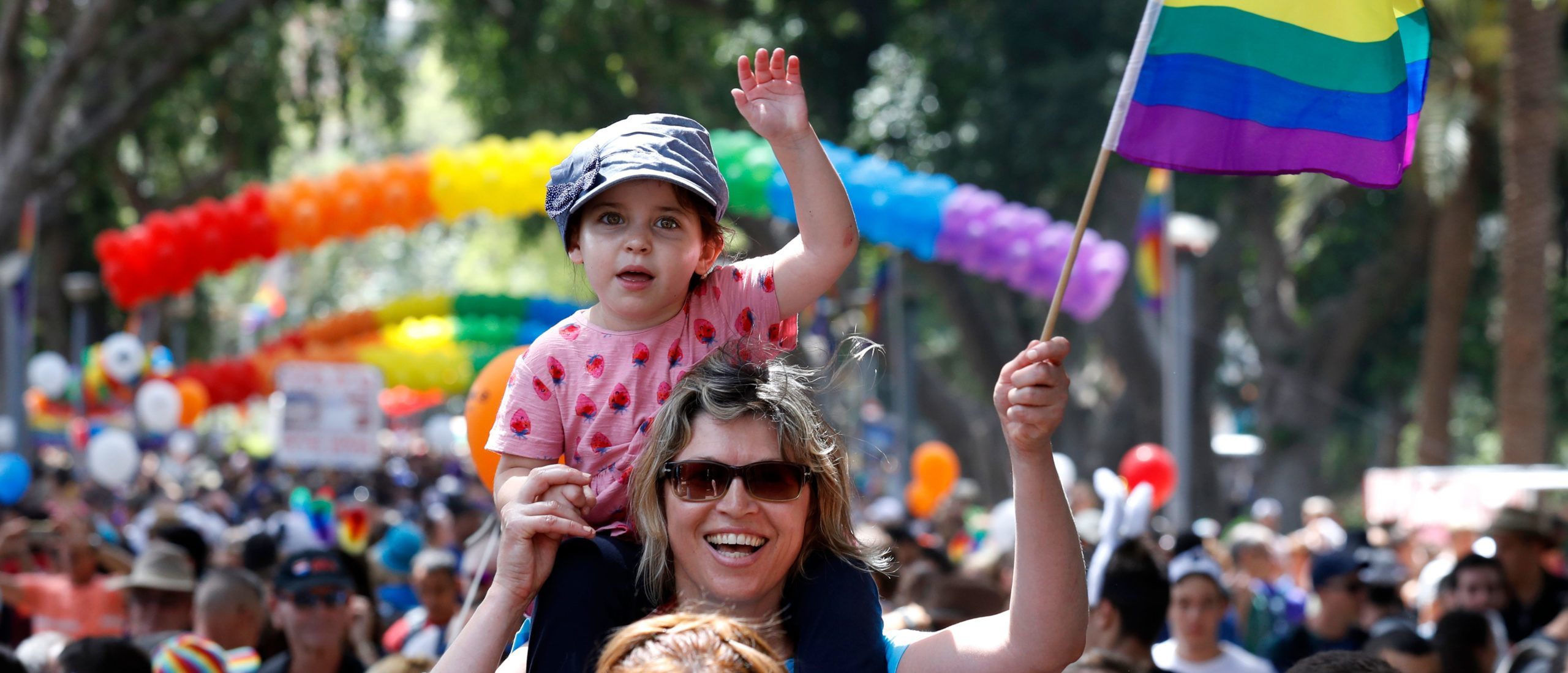A woman carrying a child on her shoulder waves a rainbow flag during the opening event of the annual Gay Pride parade in the Israeli city of Tel Aviv, on June 3, 2016. (Photo by JACK GUEZ / AFP)