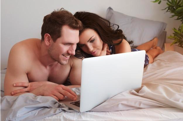 A man and a woman in bed, looking at an open laptop 