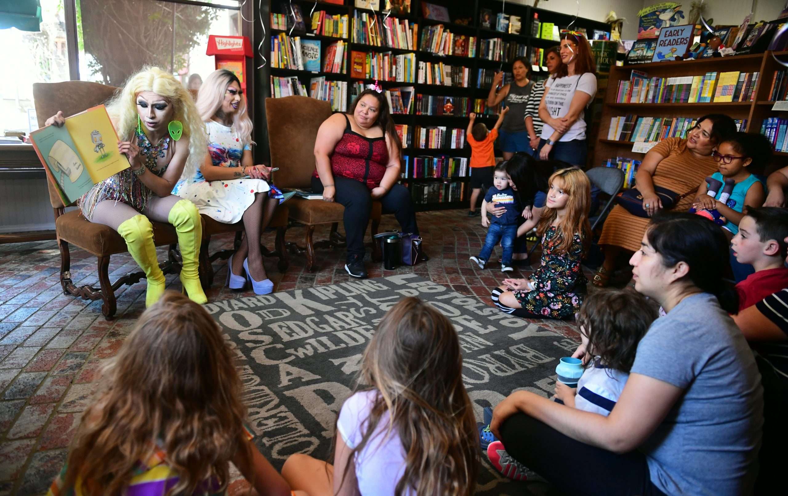 Drag queen Athena Kills (L) reads seated beside Scalene Onixxx to adults and children during Drag Queen Story Hour at Cellar Door Books in Riverside, California on June 22, 2019. - Athena and Scalene, their long blonde hair flowing down to their sequined leotards and rainbow dresses, are reading to around 15 children at a bookstore in Riverside. The scene would be unremarkable -- except that they are both drag queens. The reading workshop is part of "Drag Queen Story Hour," an initiative launched in 2015 by a handful of libraries and schools across the United States. (Photo by Frederic J. BROWN / AFP) (Photo credit should read FREDERIC J. BROWN/AFP via Getty Images)