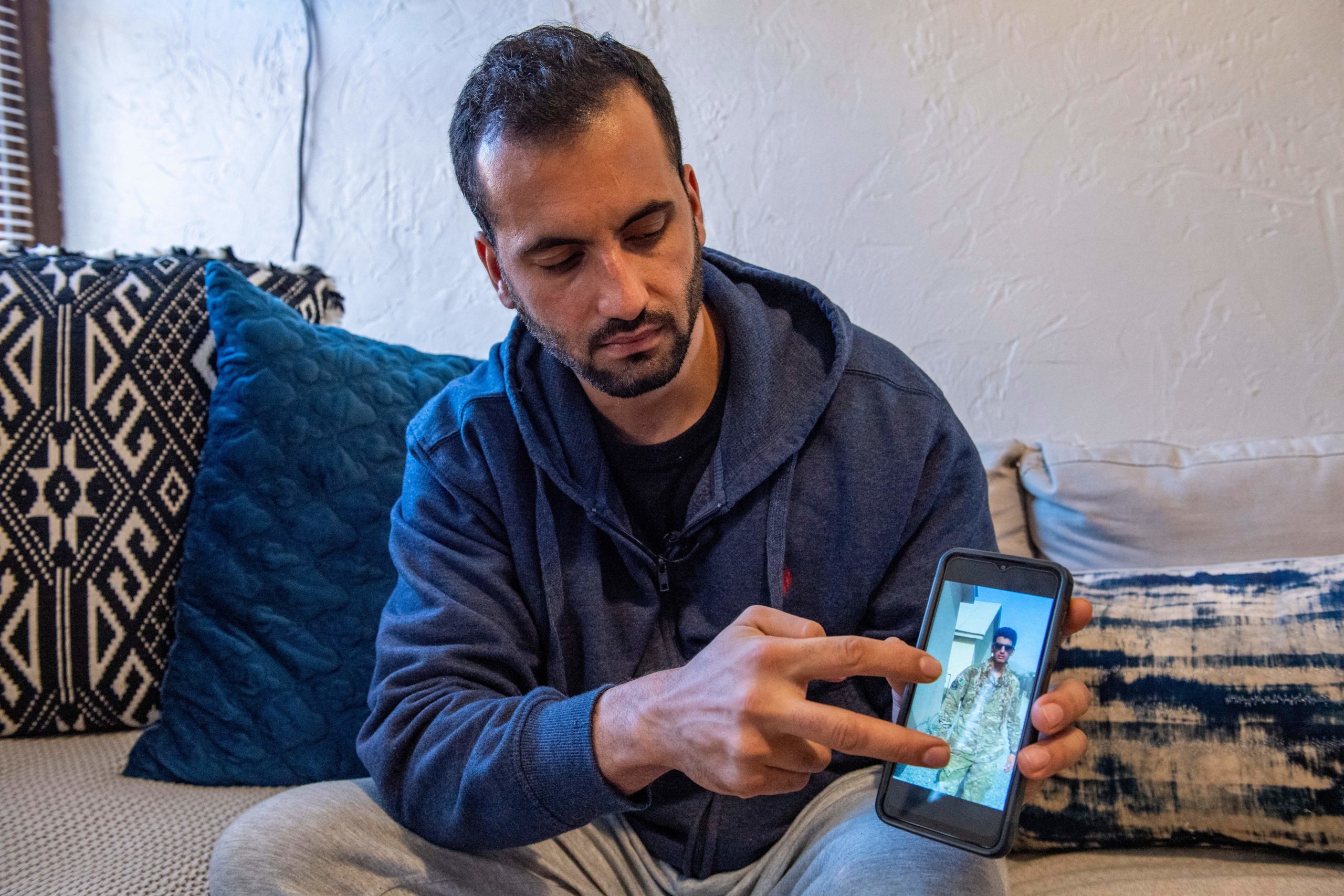 Afghani evacuee Israr, 26, points to photos on his phone of himself working in Afghanistan as a translator with military forces at his new apartment in Charlestown, Massachusetts on February 21, 2022. - In a storied corner of Boston, one of America's newest families is finding its feet months after fleeing Afghanistan: Israr and Sayeda are starting work, studying a new language and setting up home to welcome their first-born child. But like many of the tens of thousands of Afghans evacuated after Kabul's fall to the Taliban, the young couple -- who asked to be identified by first names only -- are also taking steps to ensure the rug doesn't get pulled out from under their new life. Though he worked as a US Army interpreter, Israr and his wife are in the United States on what is known as humanitarian parole, a "tenuous legal status," according to resettlement organizations, that offers only two years residence. After an arduous, months-long journey that took them from Kabul via Qatar to an army base in Texas, the pair settled early this year in Boston's Charlestown neighborhood where they were taken under the wing of a couple they now call their second "mama and papa." 