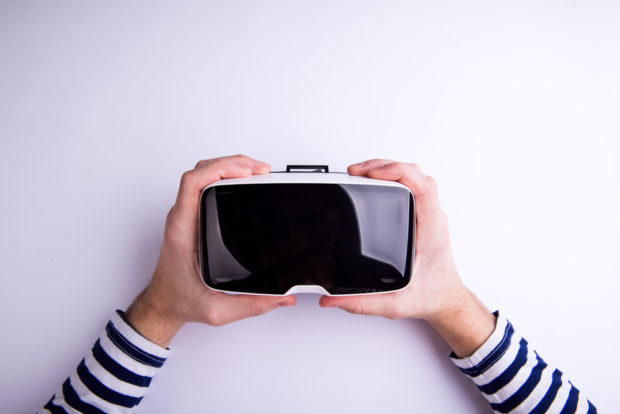 Hands of a man holding a virtual reality headset [Shutterstock Ground Picture]